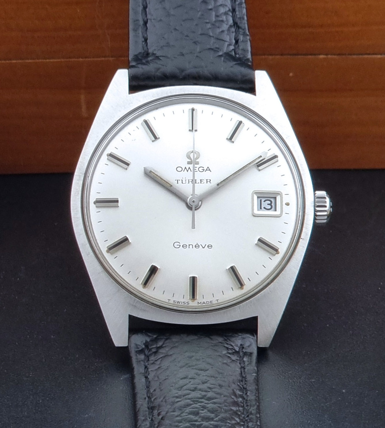 Vintage Omega watch Geneve 136.041 Co-signed Türler with a black leather strap and silver case on a dark background front view