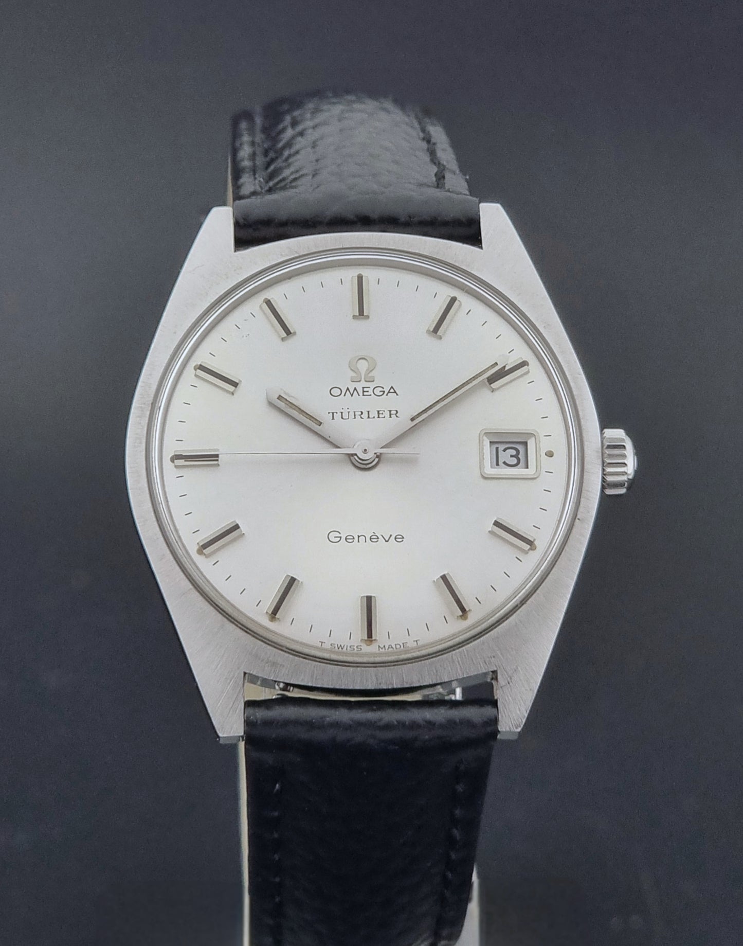 Vintage Omega watch Geneve 136.041 Co-signed Türler with a black leather strap and silver case on a dark background close dial view