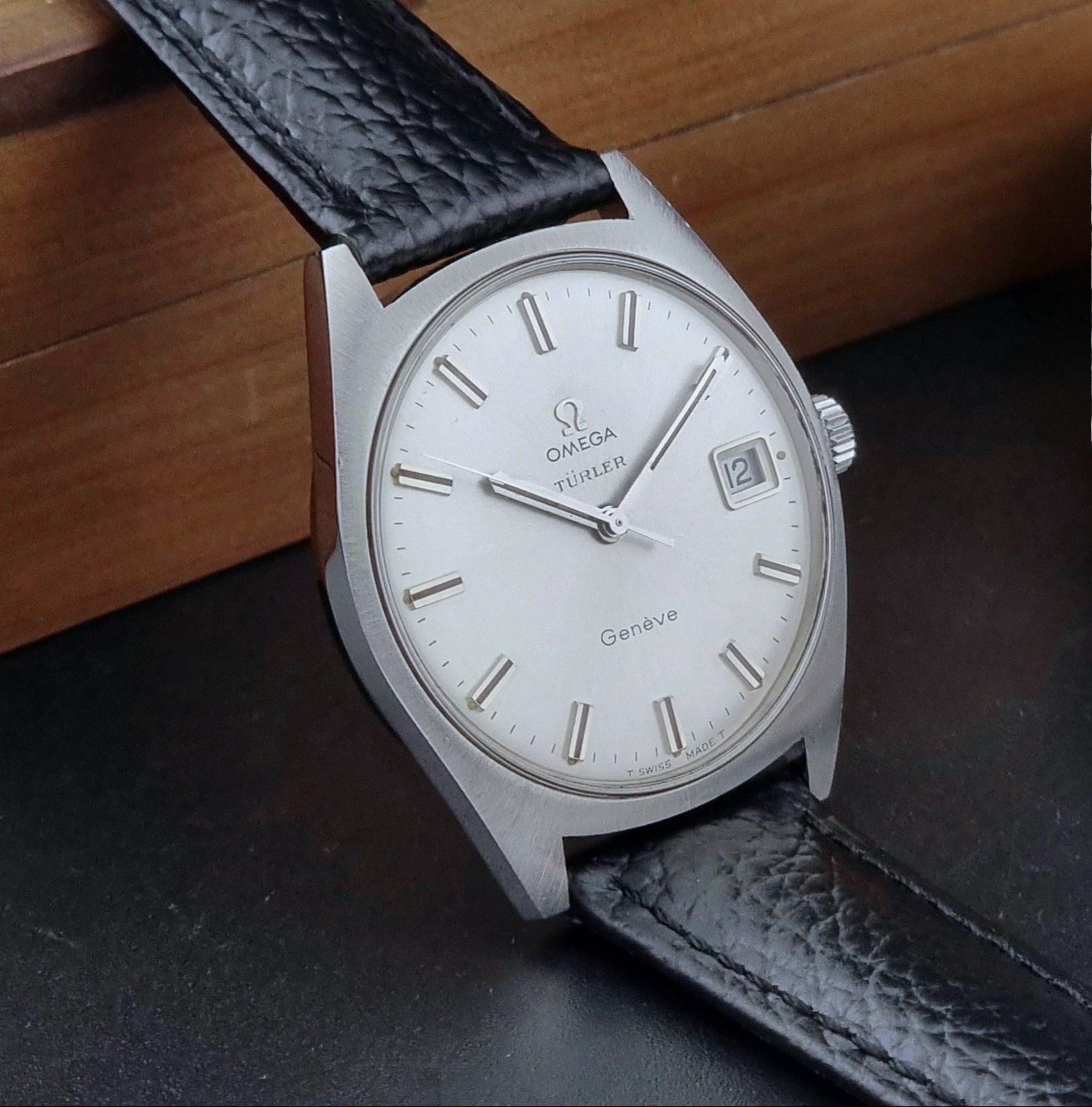 Vintage Omega watch Geneve 136.041 Co-signed Türler with a black leather strap and silver case on a dark background side view