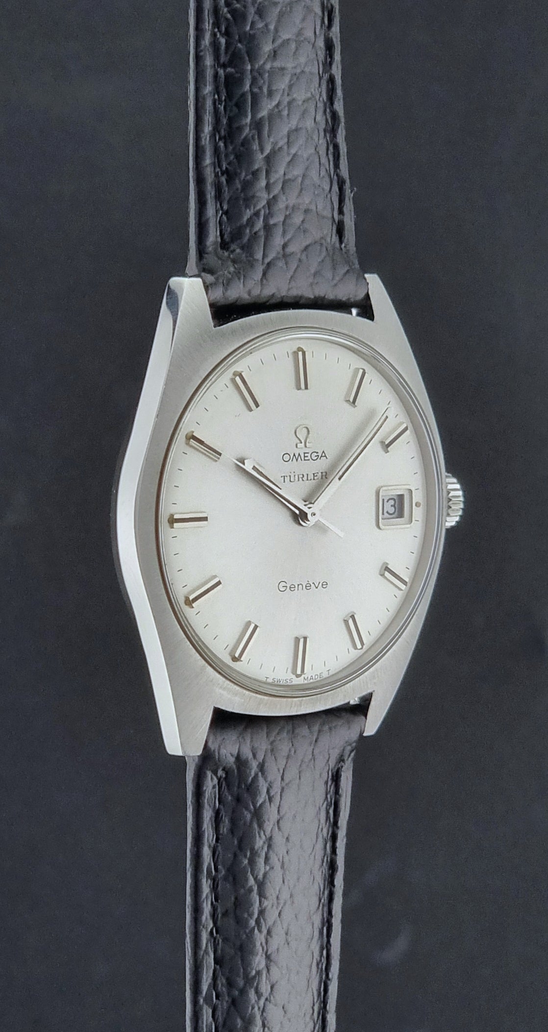 Vintage Omega watch Geneve 136.041 Co-signed Türler with a black leather strap and silver case on a dark background side profile view