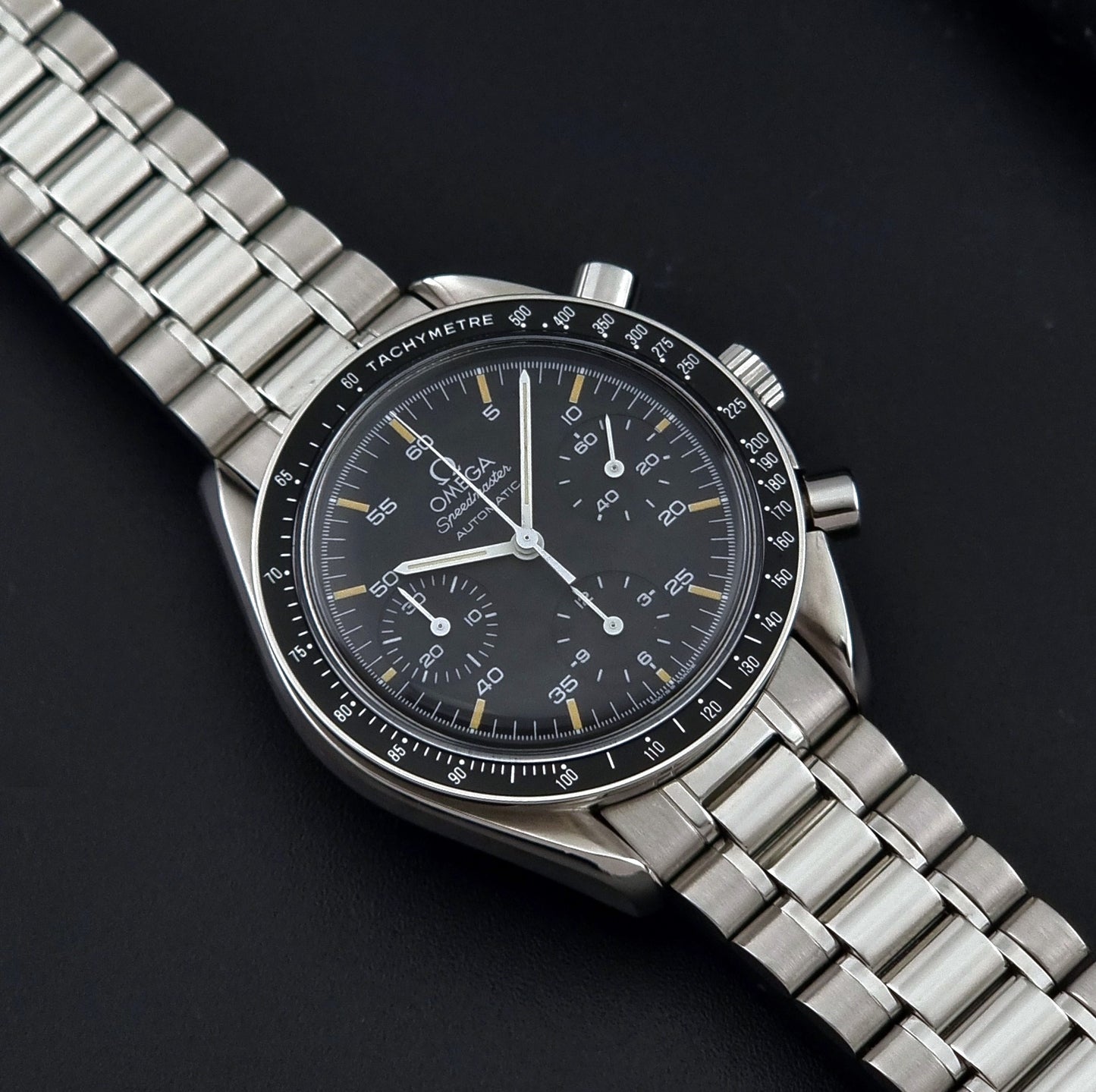 Vintage Omega watch Speedmaster Reduced 3510.50 watch with a black dial on a dark textured background close up dial view