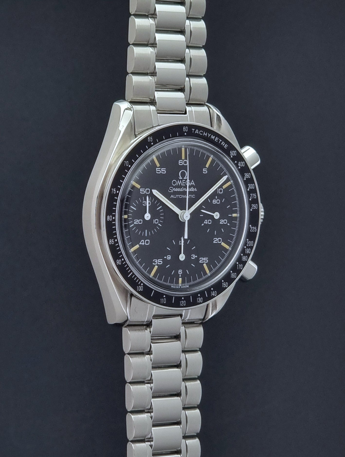Vintage Omega watch Speedmaster Reduced 3510.50 watch with a black dial on a dark textured background side profile view