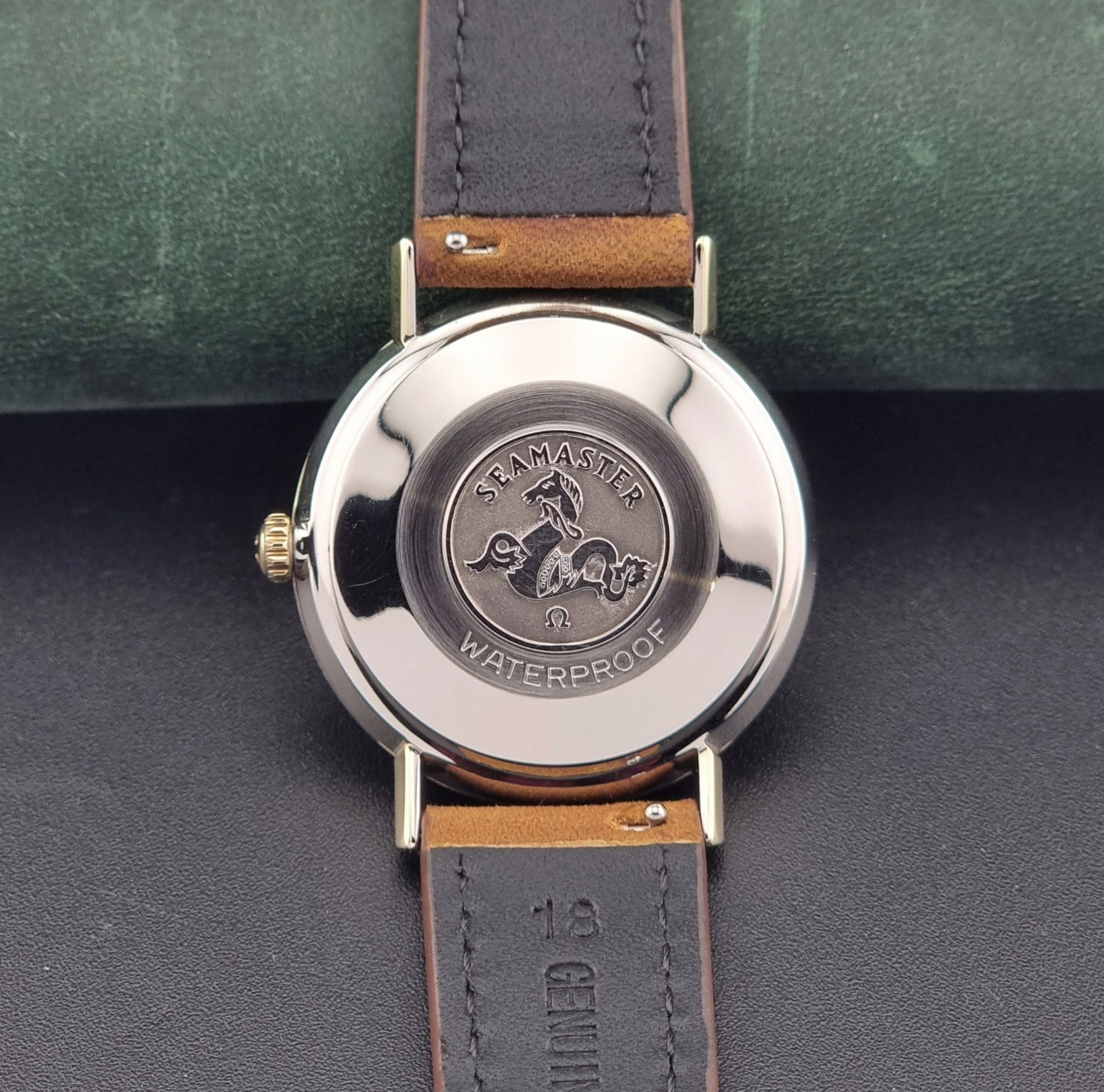 Vintage Omega Seamaster 14735 Gold watch with brown leather strap on a green textured background case back view