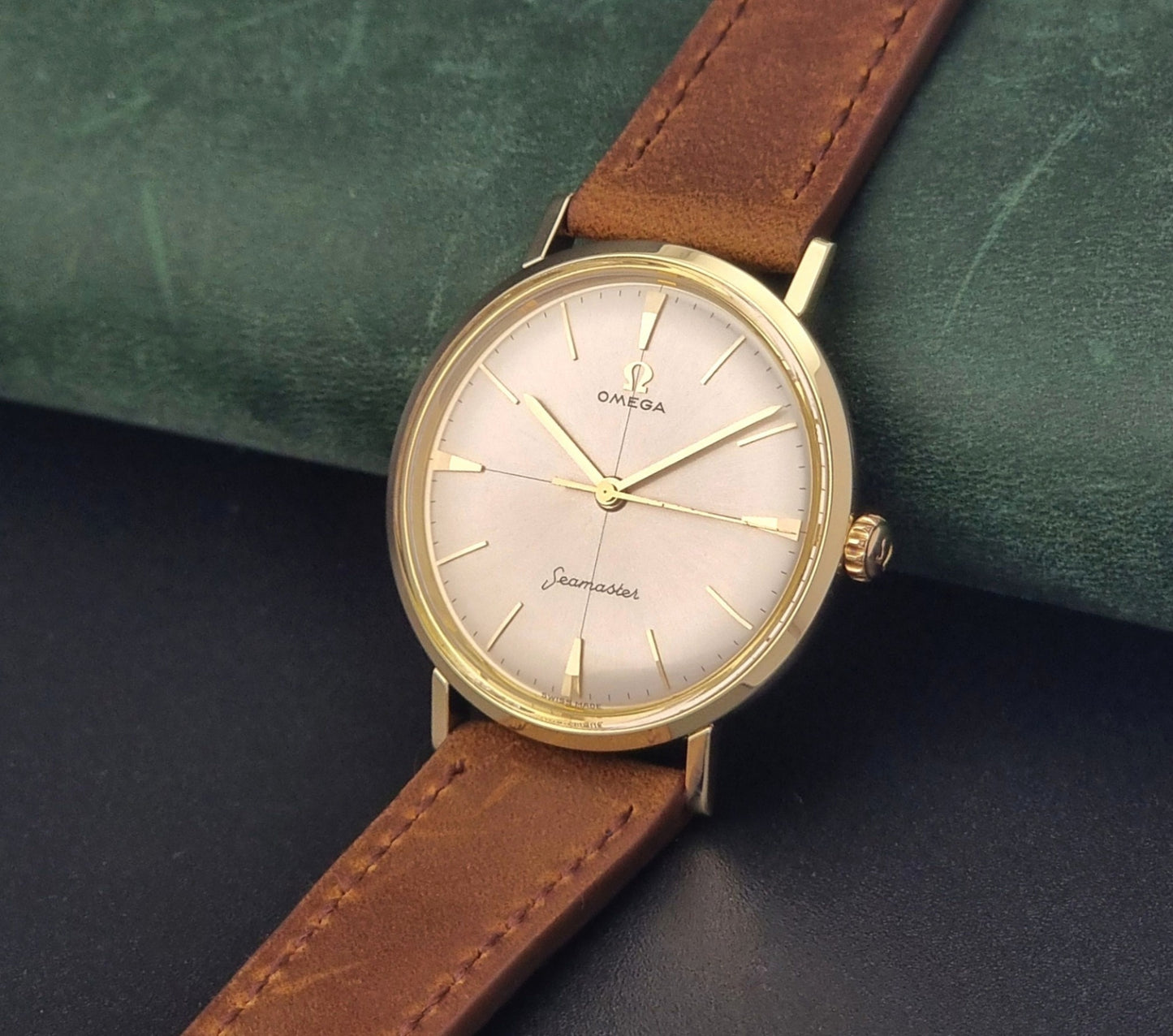 Vintage Omega Seamaster 14735 Gold watch with brown leather strap on a green textured background crown view