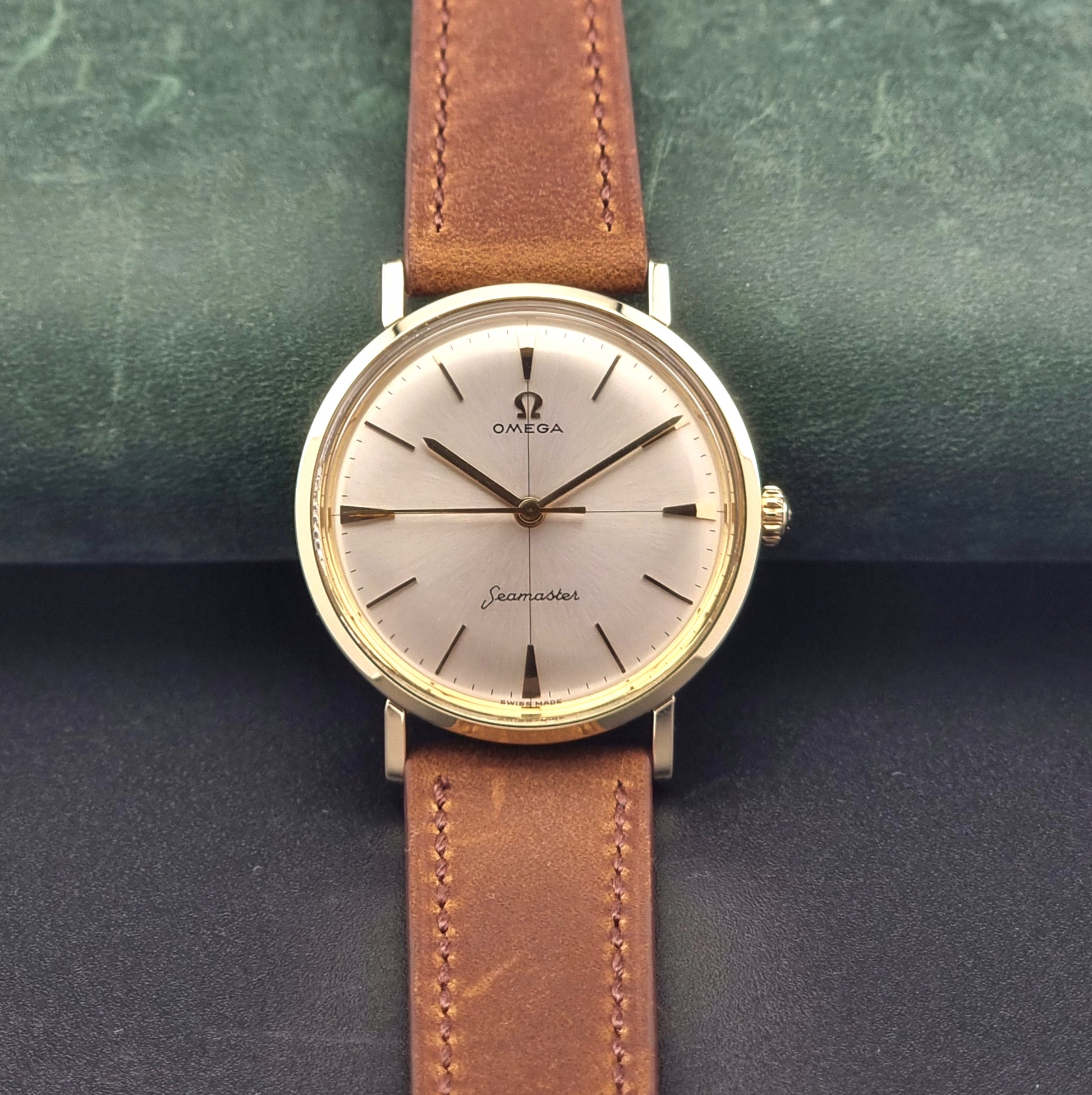 Vintage Omega Seamaster 14735 Gold watch with brown leather strap on a green textured background front view