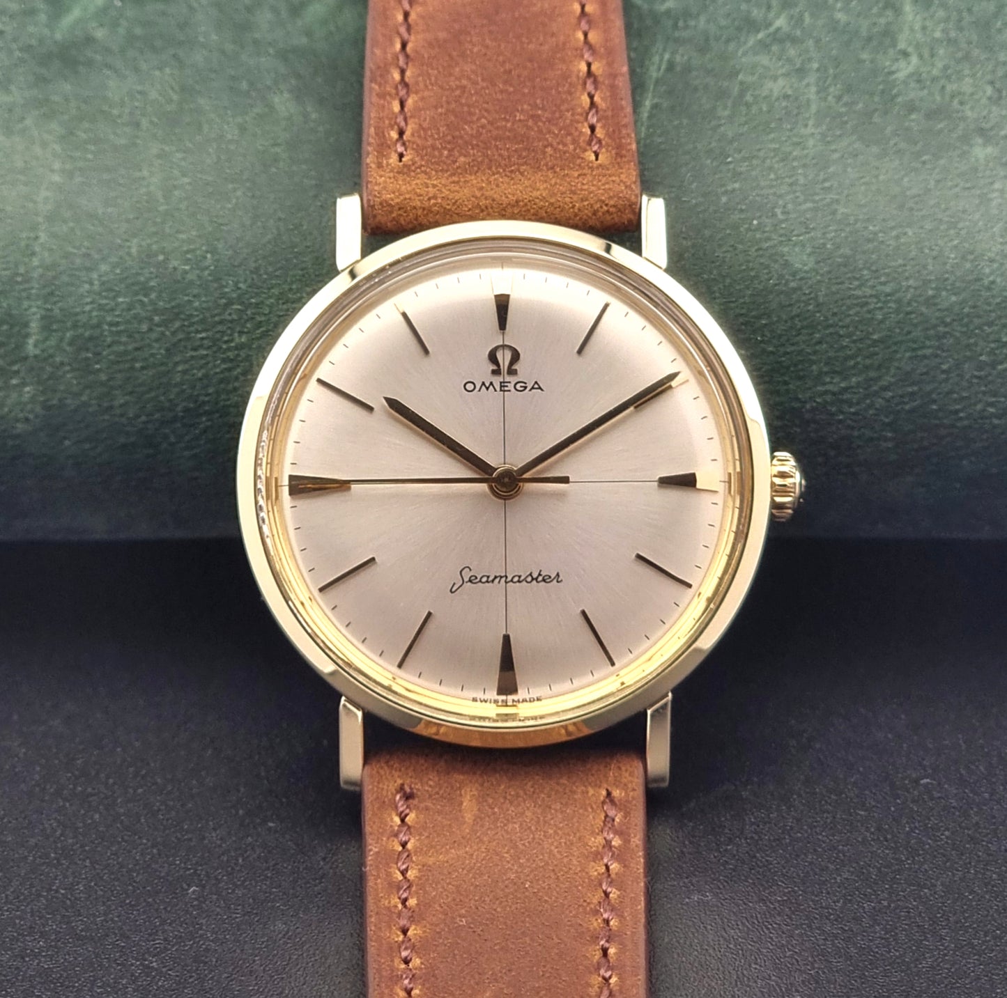 Vintage Omega Seamaster 14735 Gold watch with brown leather strap on a green textured background close up dial view