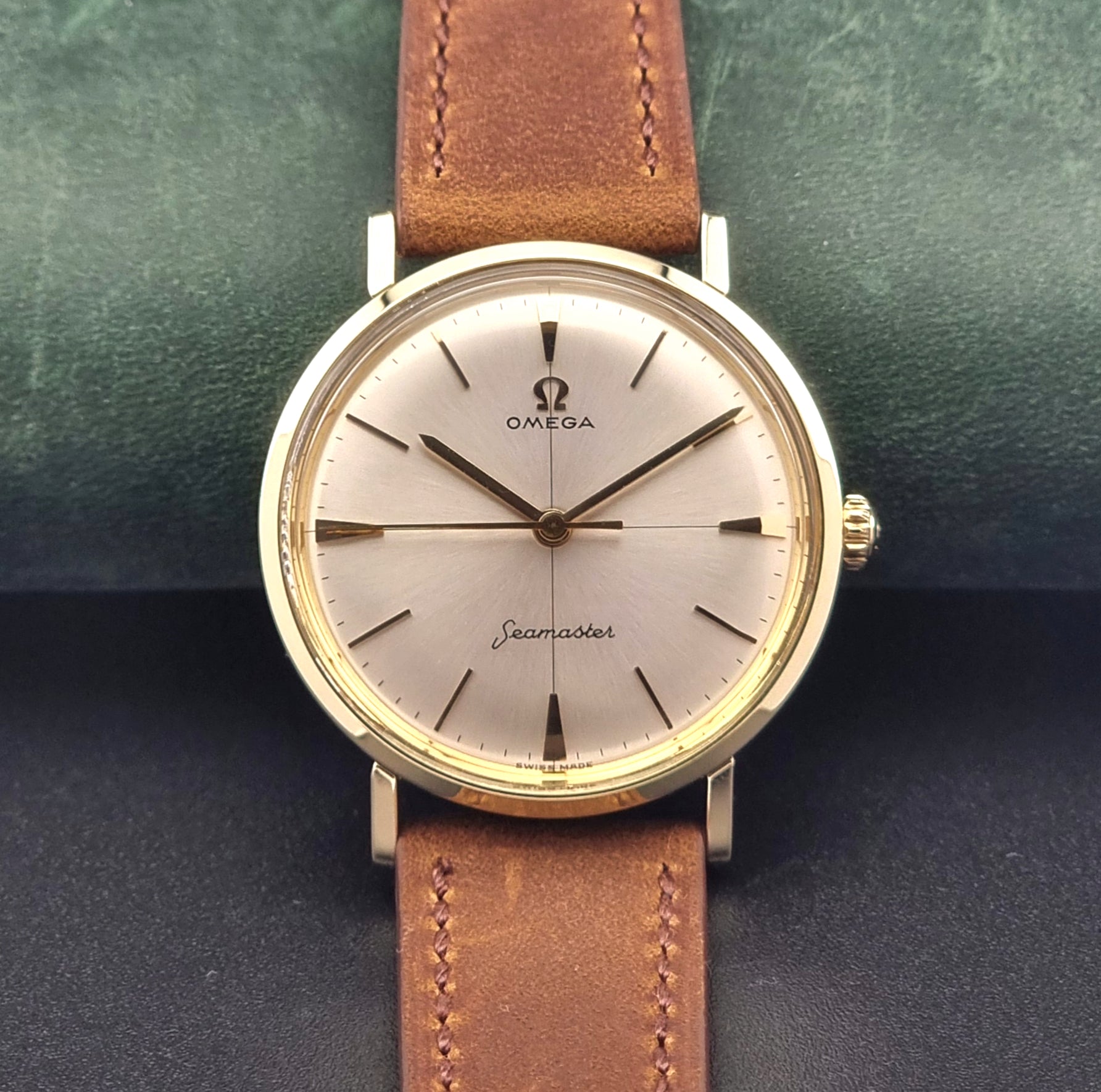Vintage Omega Seamaster 14735 Gold watch with brown leather strap on a green textured background close up dial view