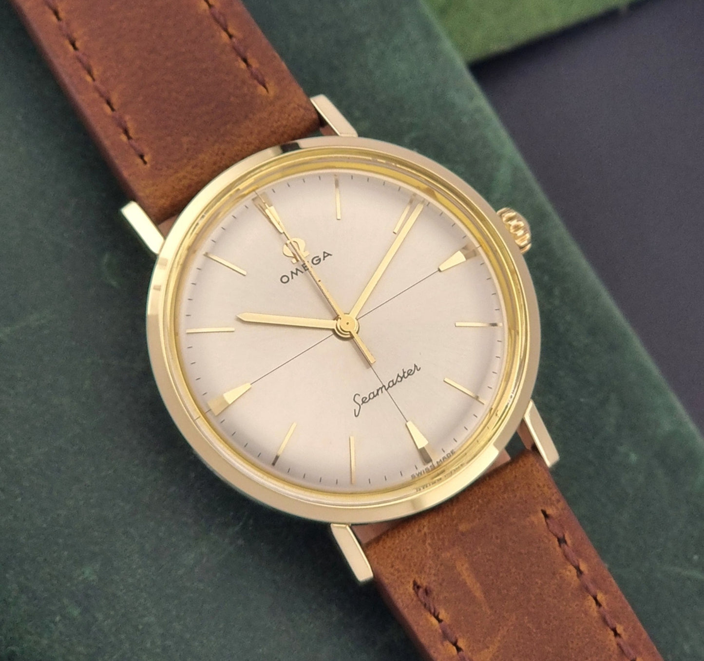 Vintage Omega Seamaster 14735 Gold watch with brown leather strap on a green textured background close dial view
