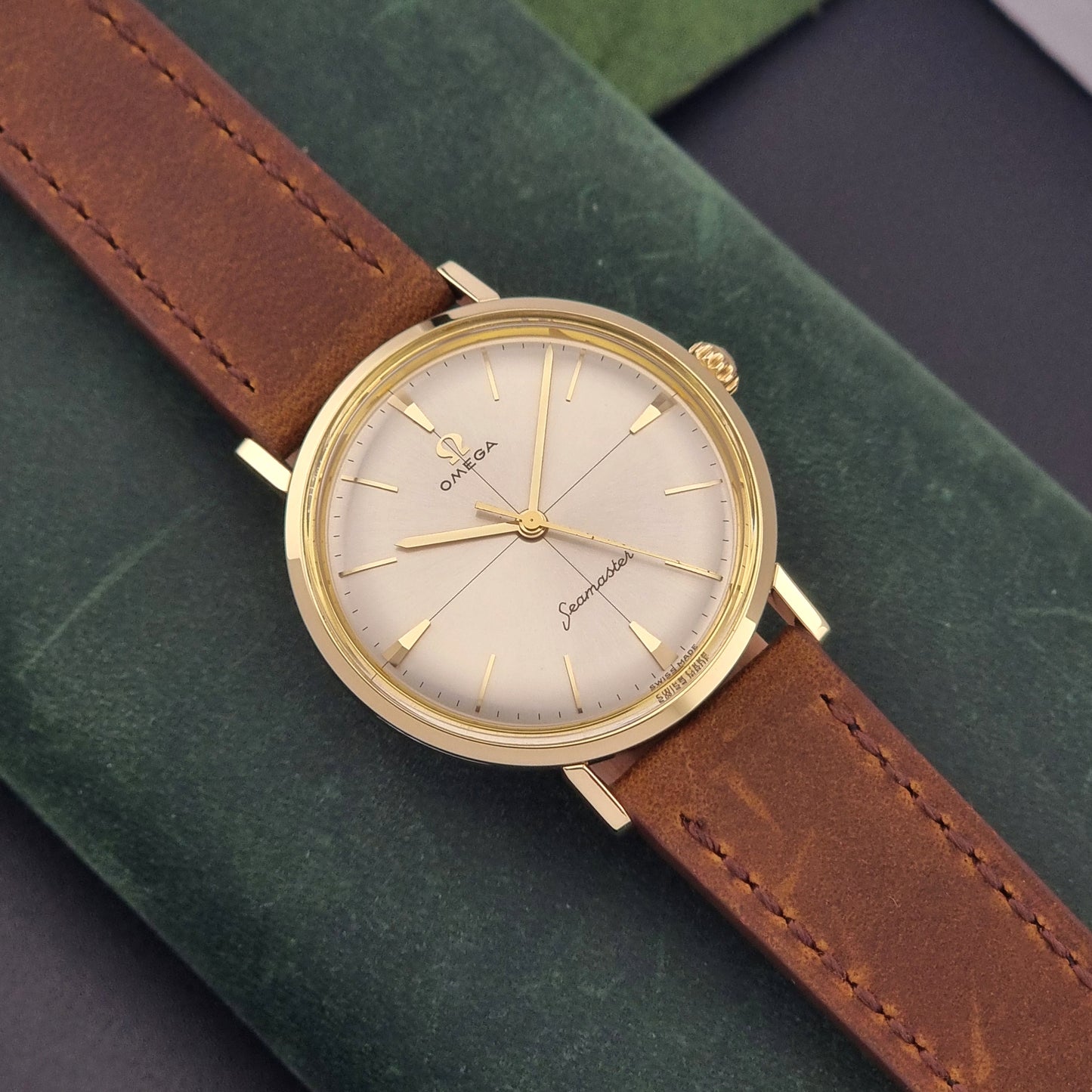 Vintage Omega Seamaster 14735 Gold watch with brown leather strap on a green textured background