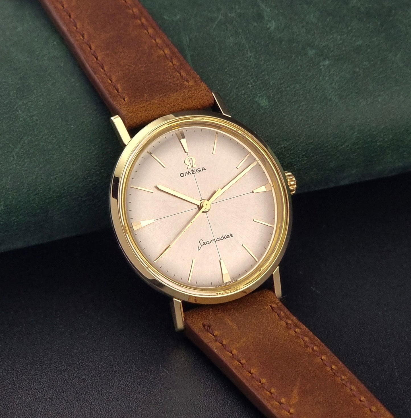 Vintage Omega Seamaster 14735 Gold watch with brown leather strap on a green textured background side view