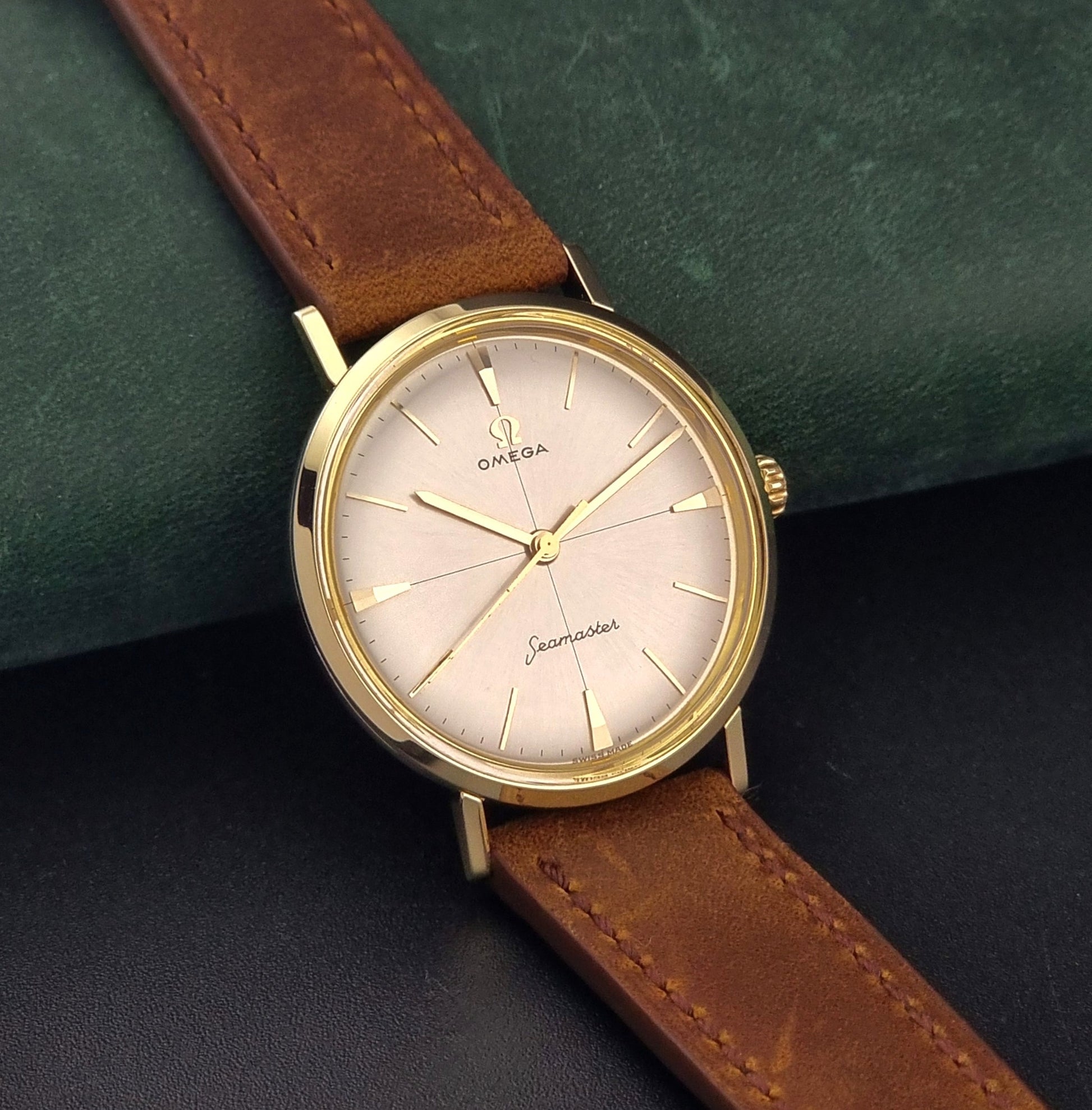 Vintage Omega Seamaster 14735 Gold watch with brown leather strap on a green textured background side view