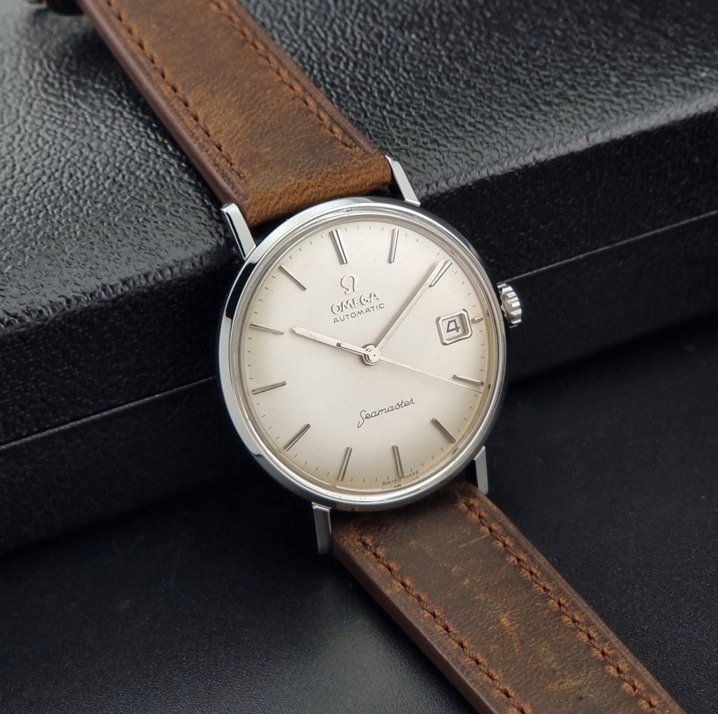 Vintage Omega Seamaster 14770 watch with a brown leather strap on a dark background side view
