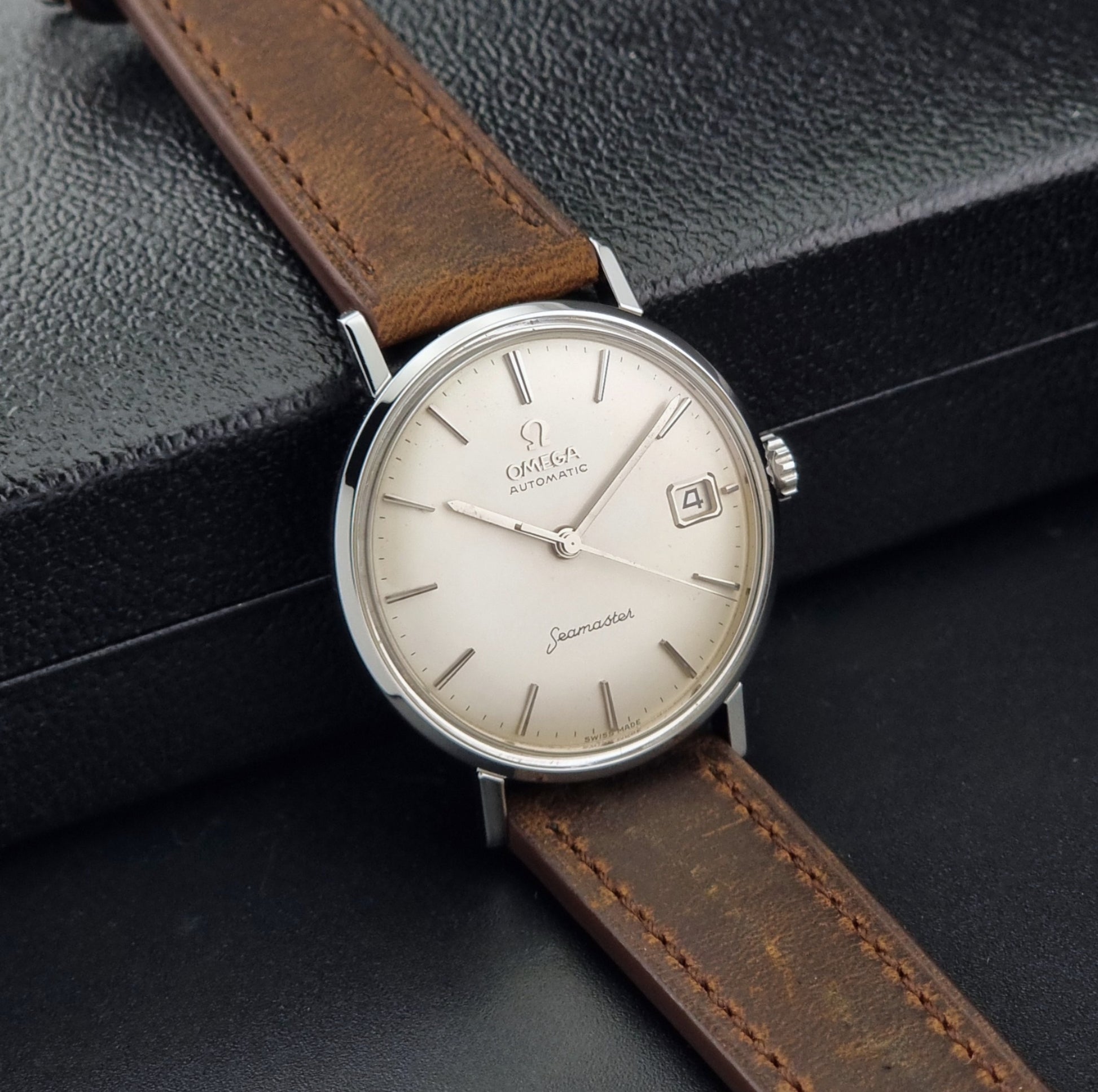 Vintage Omega Seamaster 14770 watch with a brown leather strap on a dark background side view