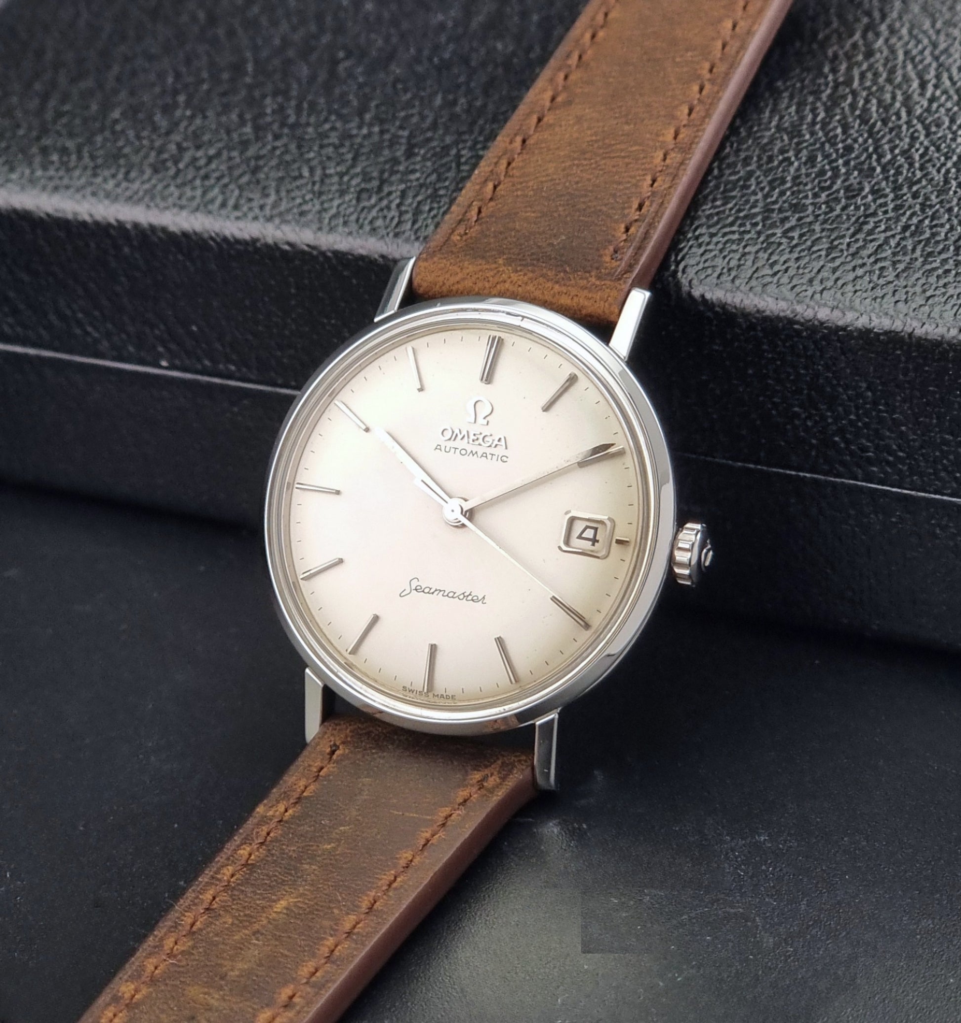 Vintage Omega Seamaster 14770 watch with a brown leather strap on a dark background crown view
