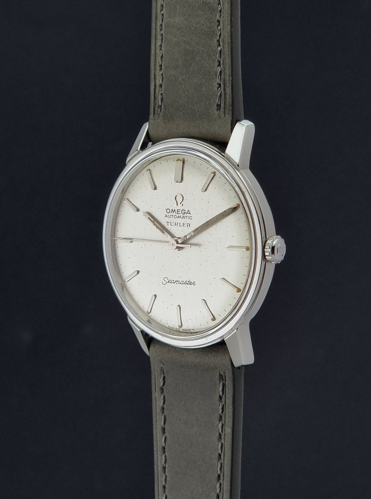 Vintage Omega Wristwatch Seamaster Turler 165.002 with a silver-toned oval case, white dial, and grey leather strap, shown against a dark background.