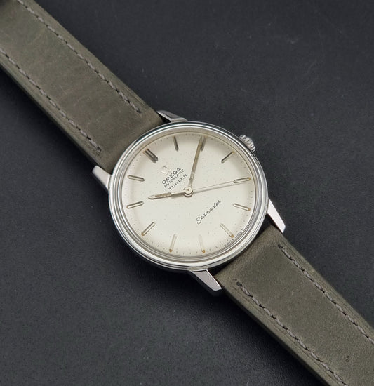 Vintage Omega Wristwatch Seamaster Turler 165.002 with a silver-toned case, cream-colored dial, and olive green leather strap, shown on a dark textured background.
