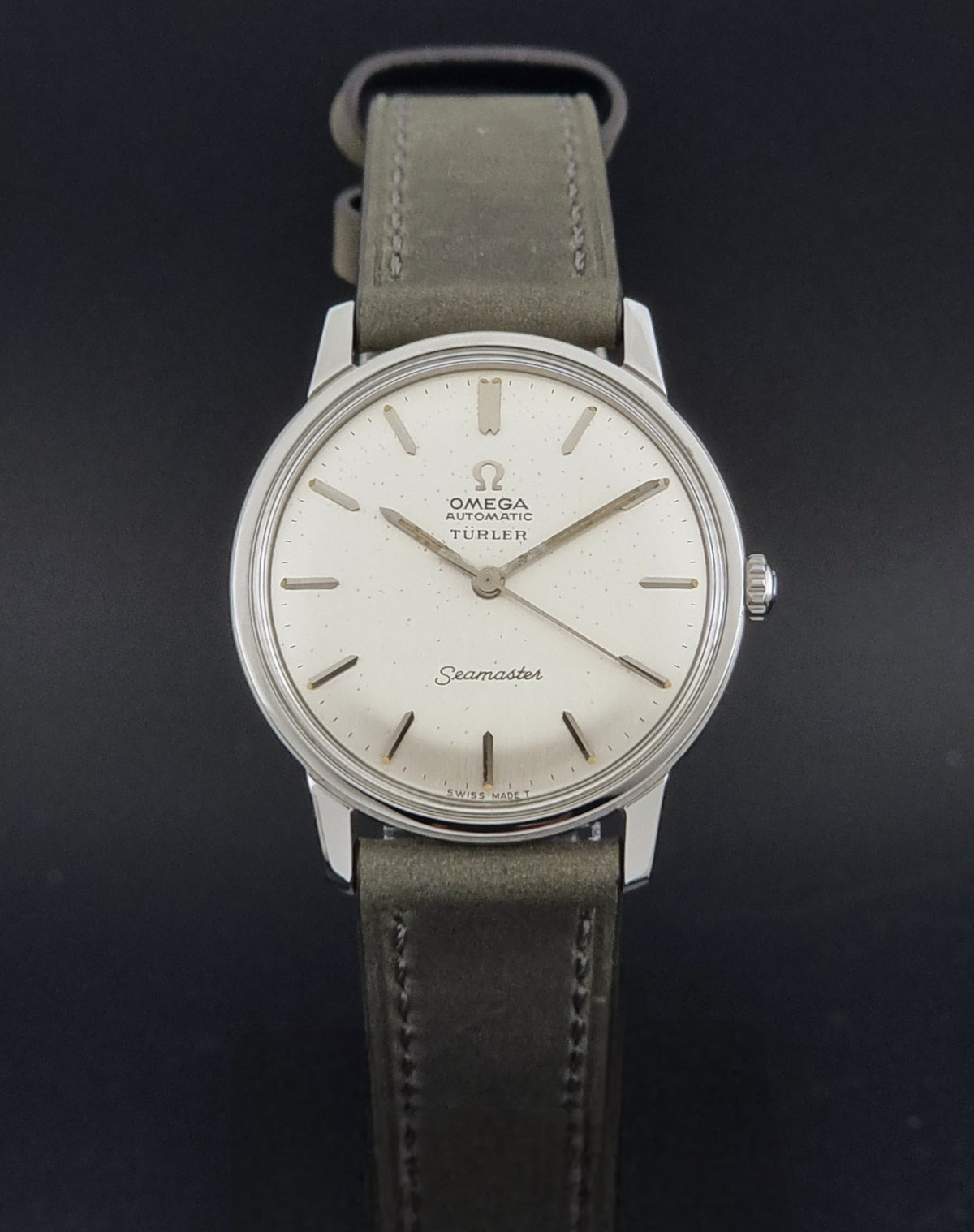 Vintage Omega Wristwatch Seamaster Turler 165.002 with a silver-toned case, cream dial, and grey leather strap, shown against a dark background.