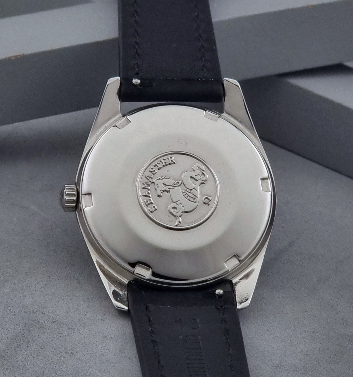Vintage Omega Wristwatch Seamaster 166.010 with black leather strap on a gray background case back view