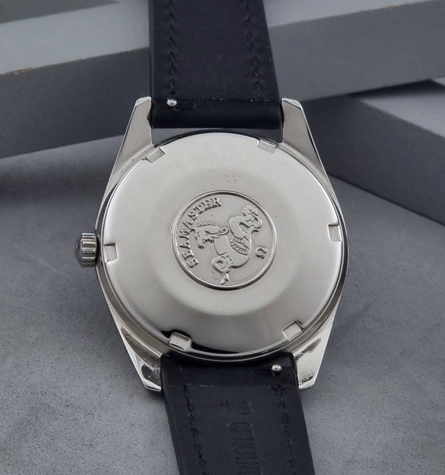Vintage Omega Wristwatch Seamaster 166.010 with black leather strap on a gray background case back view