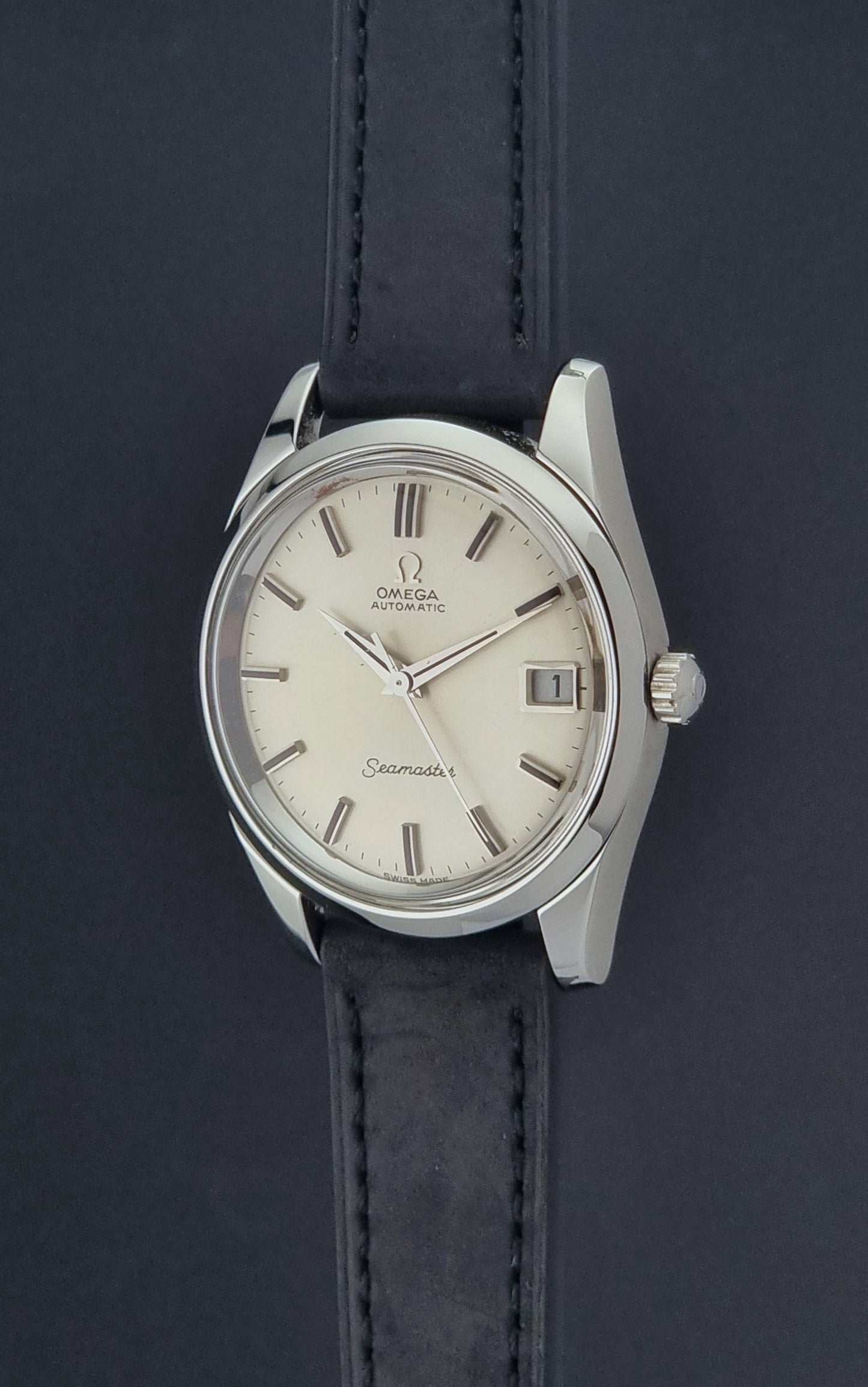 Vintage Omega Wristwatch Seamaster 166.010 with black leather strap on a gray background crown profile view