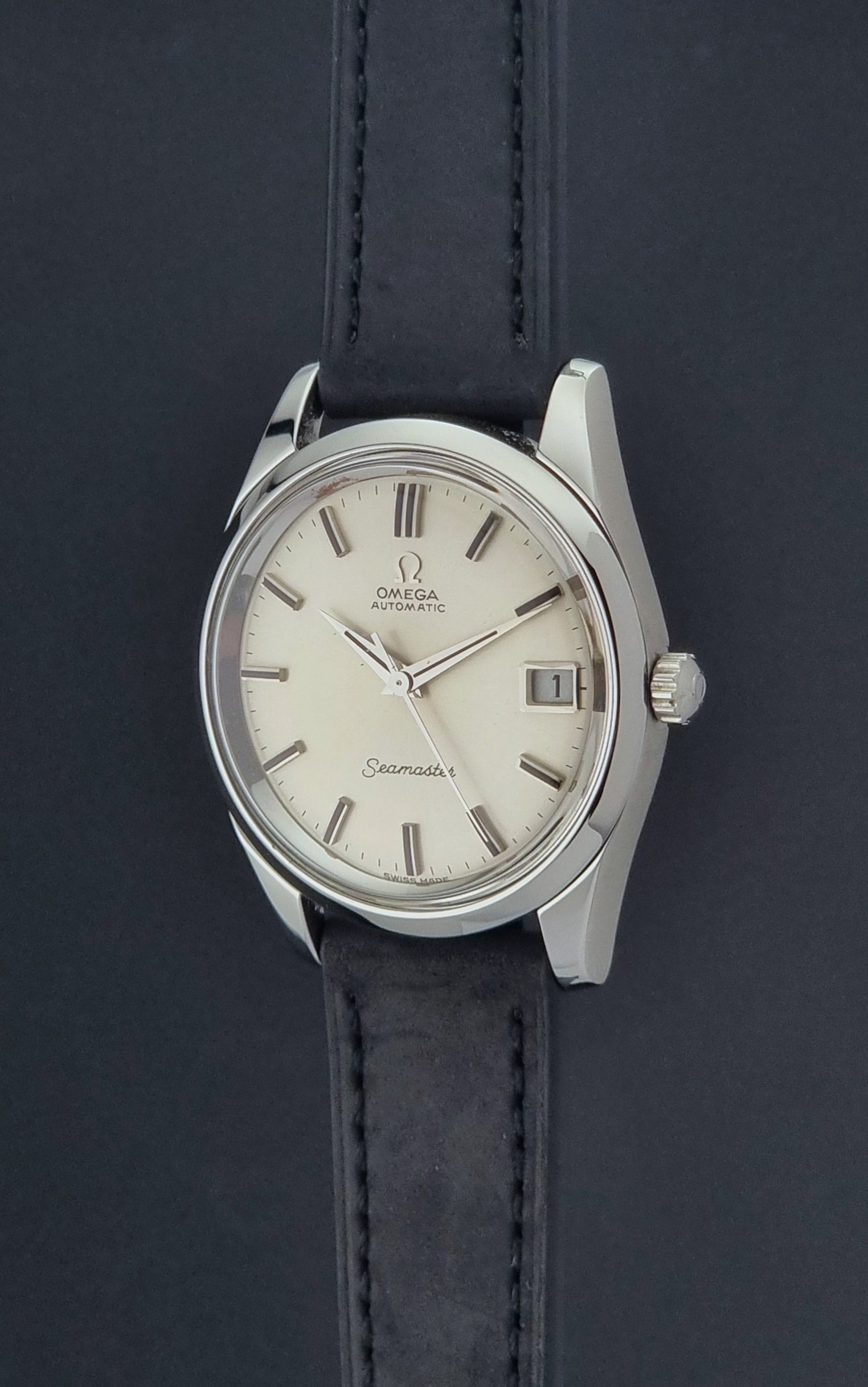 Vintage Omega Wristwatch Seamaster 166.010 with black leather strap on a gray background crown profile view