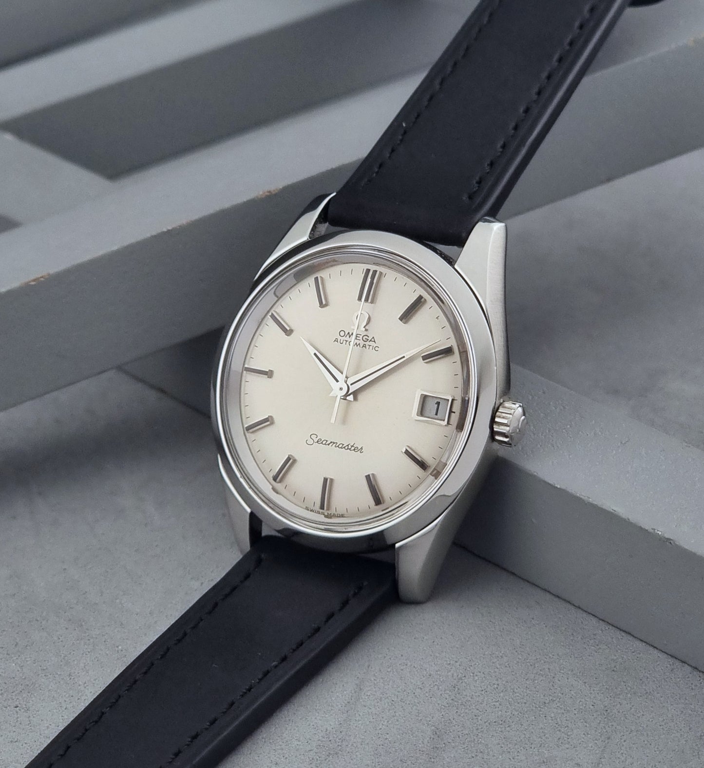 Vintage Omega Wristwatch Seamaster 166.010 with black leather strap on a gray background crown view