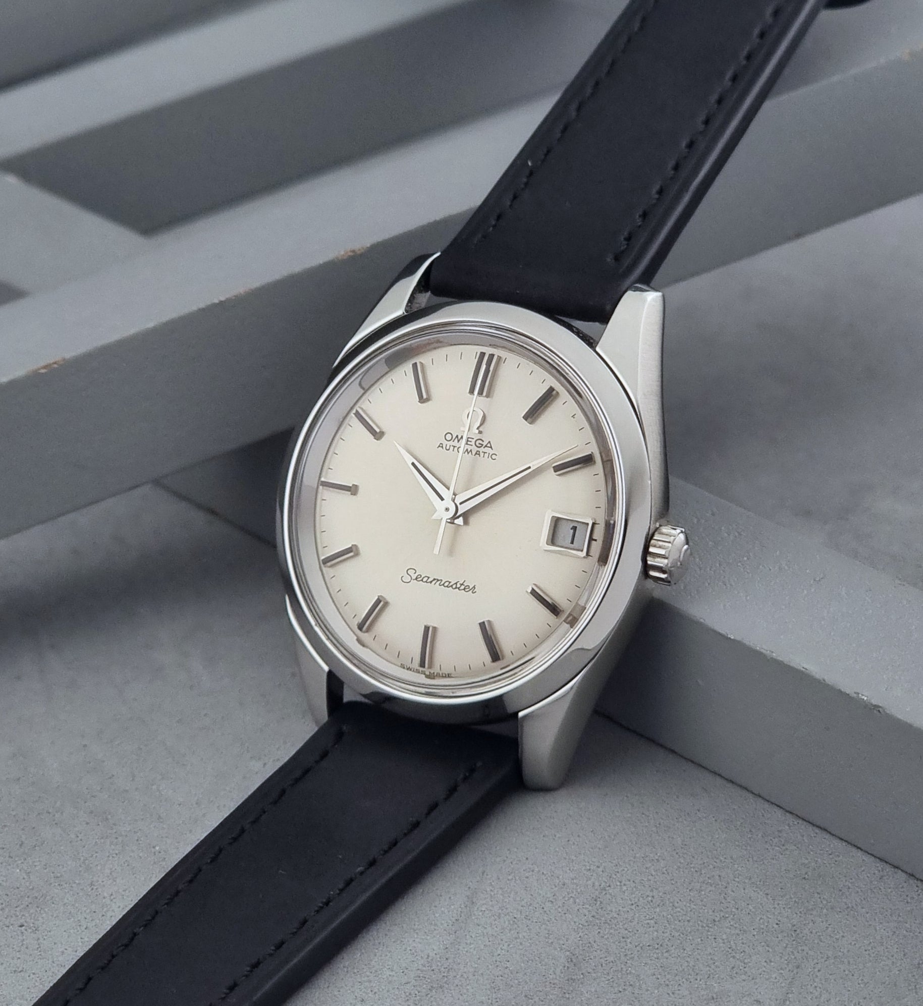 Vintage Omega Wristwatch Seamaster 166.010 with black leather strap on a gray background crown view