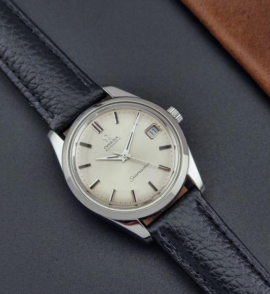 Vintage Omega Seamaster 166.010 watch with a silver dial and black leather strap on a dark surface