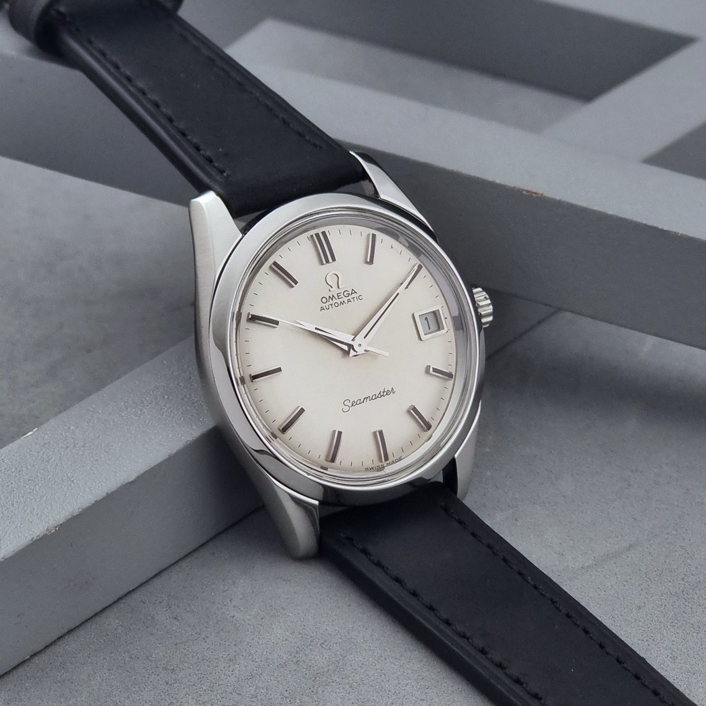 Vintage Omega Wristwatch Seamaster 166.010 with black leather strap on a gray background side view