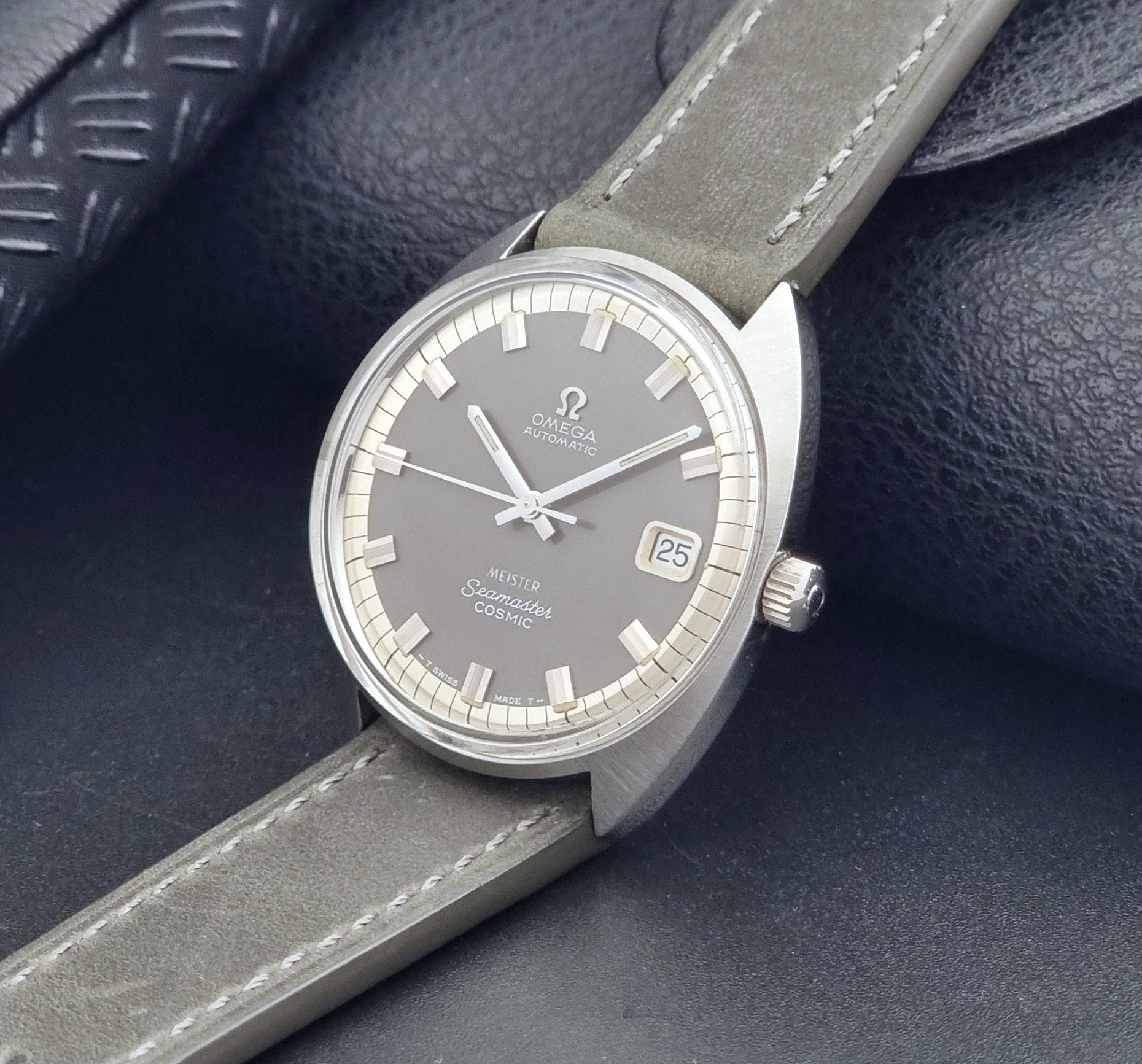 Vintage Omega Seamaster Cosmic 166.026 Wristwatch Meister Dial with leather strap on a dark gray background crown view