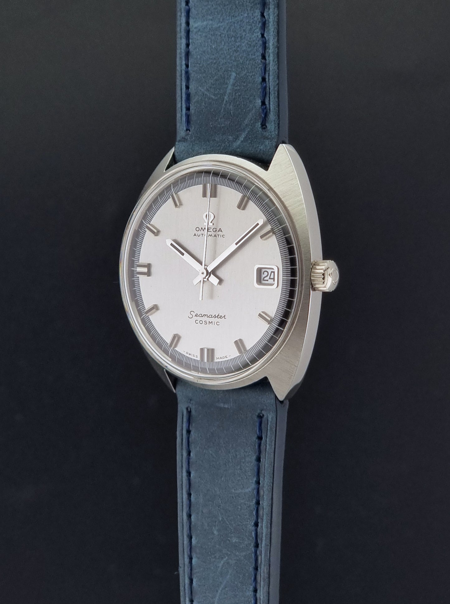 Vintage Omega 166.026 Seamaster Cosmic Wristwatch with blue leather strap and silver case on a dark gray background crown profile view