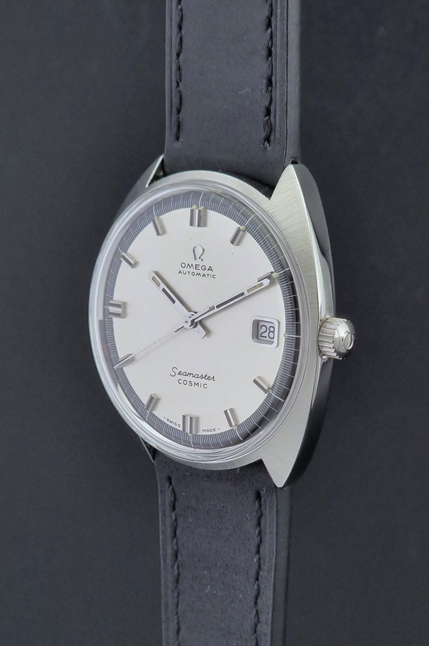 Vintage Omega Wristwatch Seamaster Cosmic 166.026 with silver dial and black leather strap on a gray background crown side profile