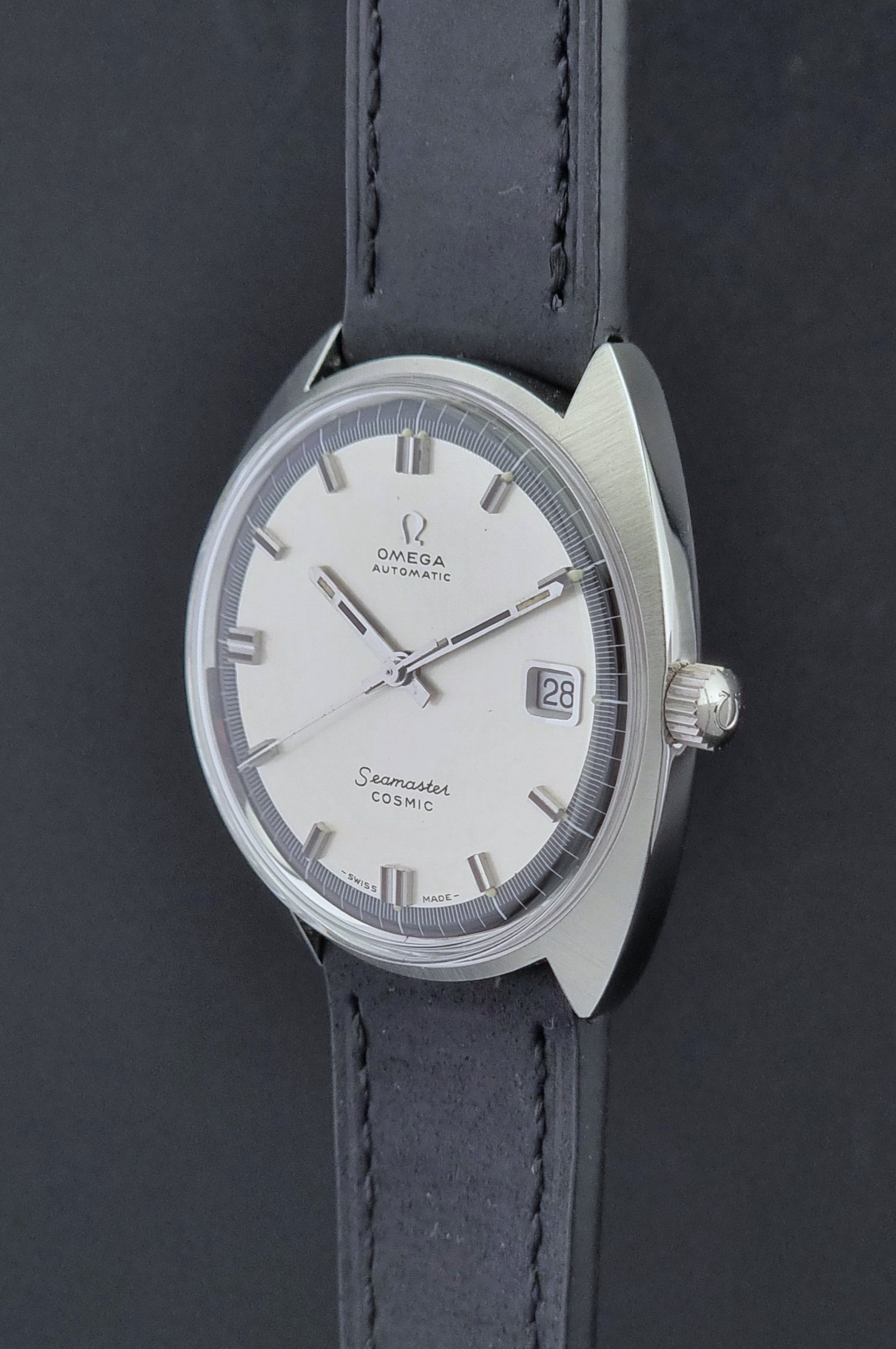 Vintage Omega Wristwatch Seamaster Cosmic 166.026 with silver dial and black leather strap on a gray background crown side profile