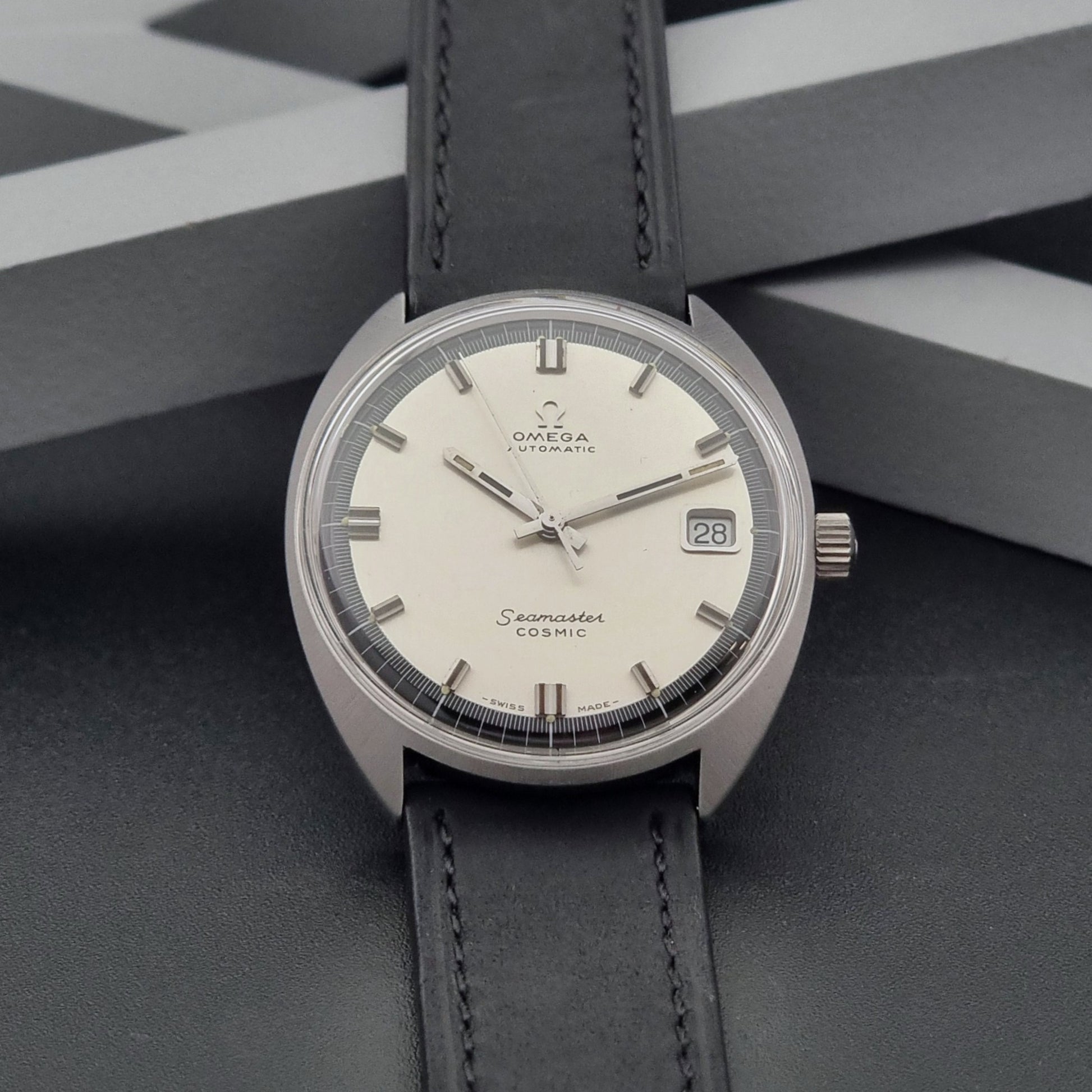 Vintage Omega Wristwatch Seamaster Cosmic 166.026 with a white face and black leather strap on a gray background
