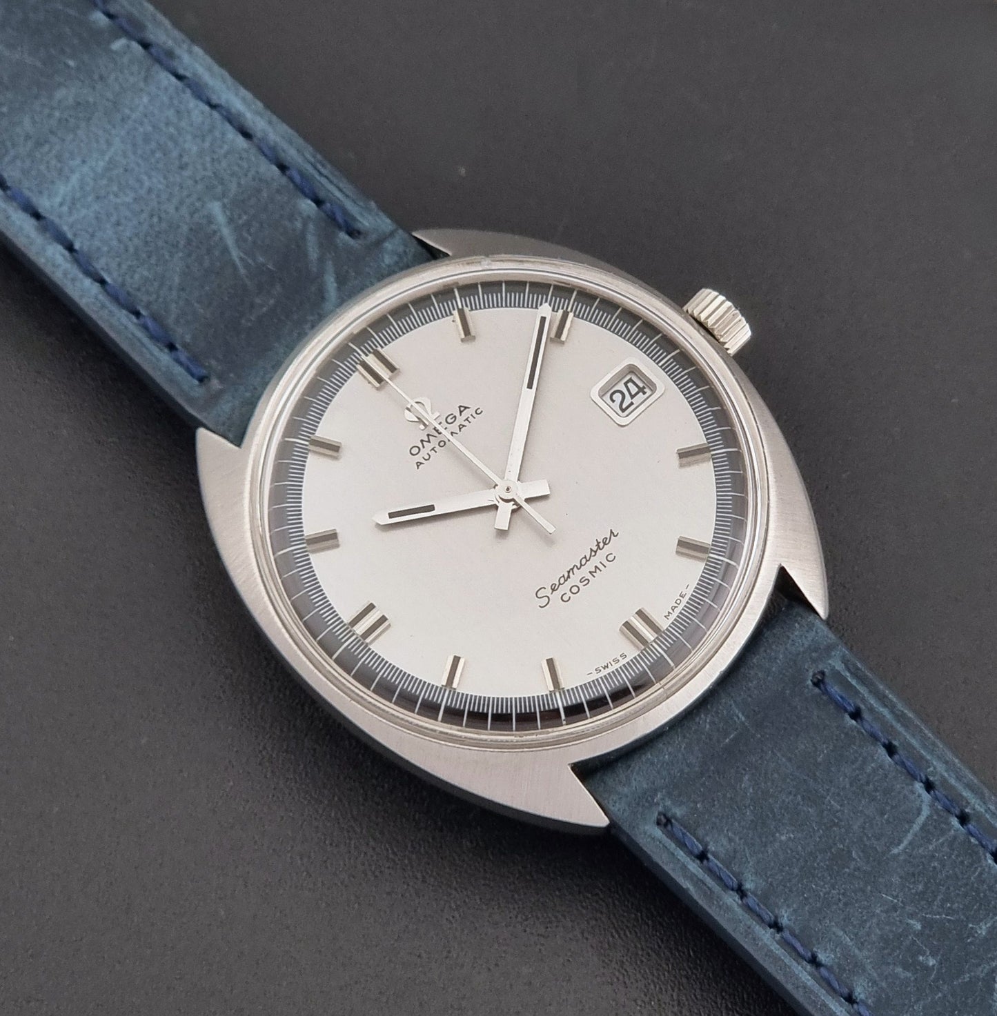 Vintage Omega 166.026 Seamaster Cosmic Wristwatch with blue leather strap and silver case on a dark gray background close up dial view