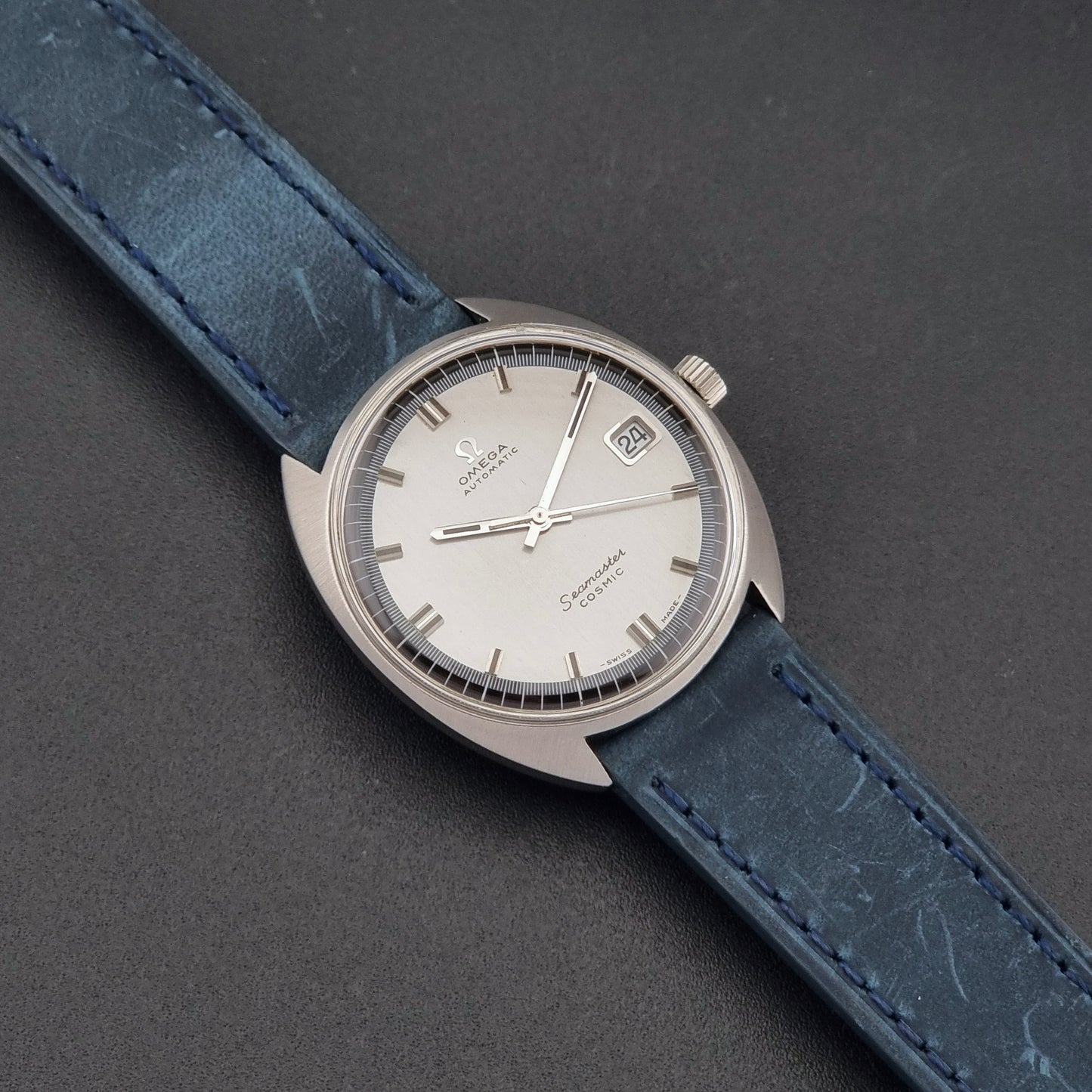 Vintage Omega 166.026 Seamaster Cosmic Wristwatch with blue leather strap and silver case on a dark gray background dial