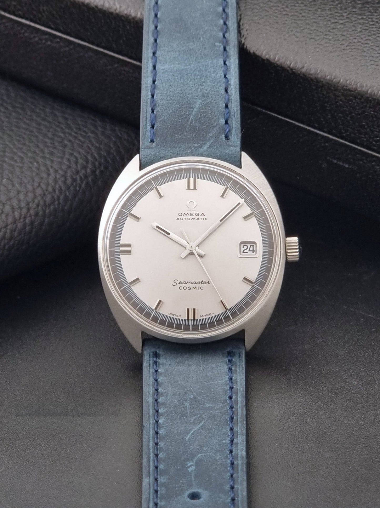 Vintage Omega 166.026 Seamaster Cosmic Wristwatch with blue leather strap and silver case on a dark gray background dial view