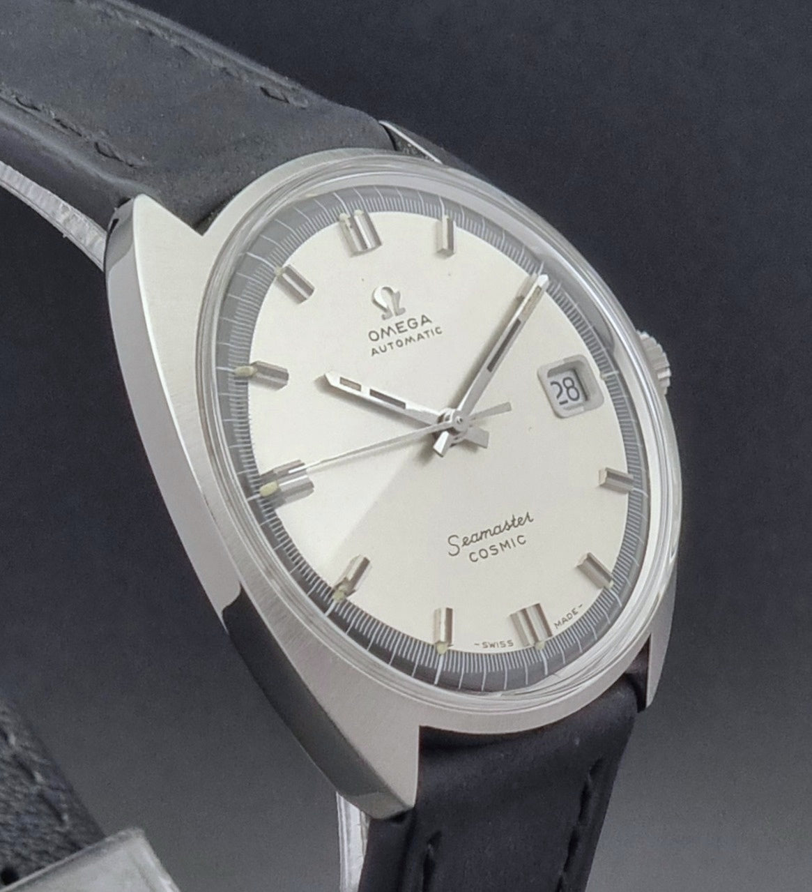 Vintage Omega Wristwatch Seamaster Cosmic 166.026 with silver dial and black leather strap on a gray background profile view