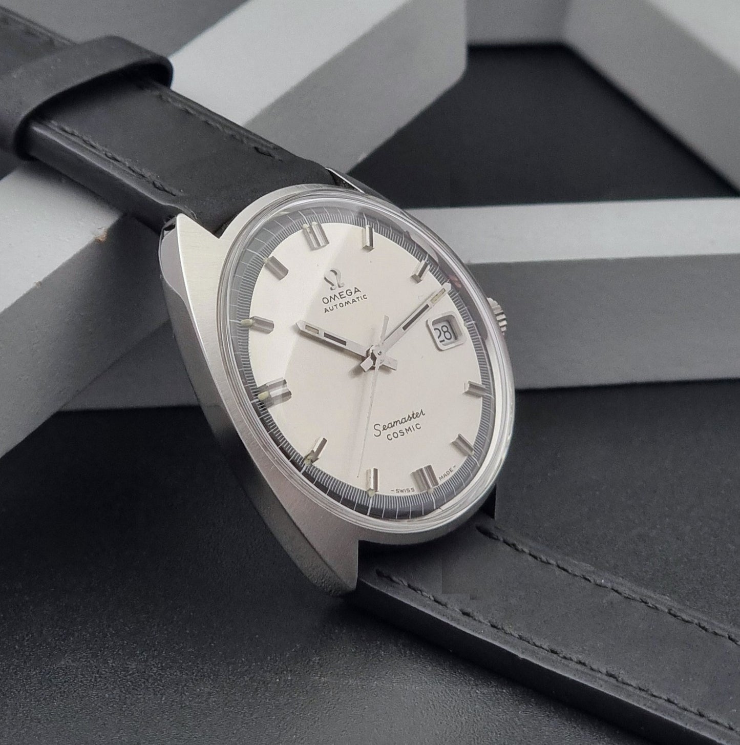 Vintage Omega Wristwatch Seamaster Cosmic 166.026 with silver dial and black leather strap on a gray background side view