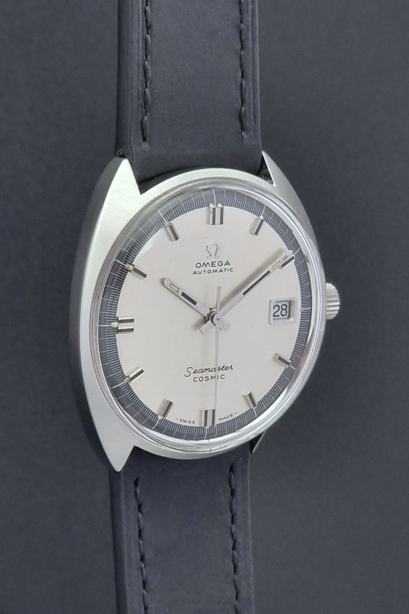 Vintage Omega Wristwatch Seamaster Cosmic 166.026 with silver dial and black leather strap on a gray background side profile