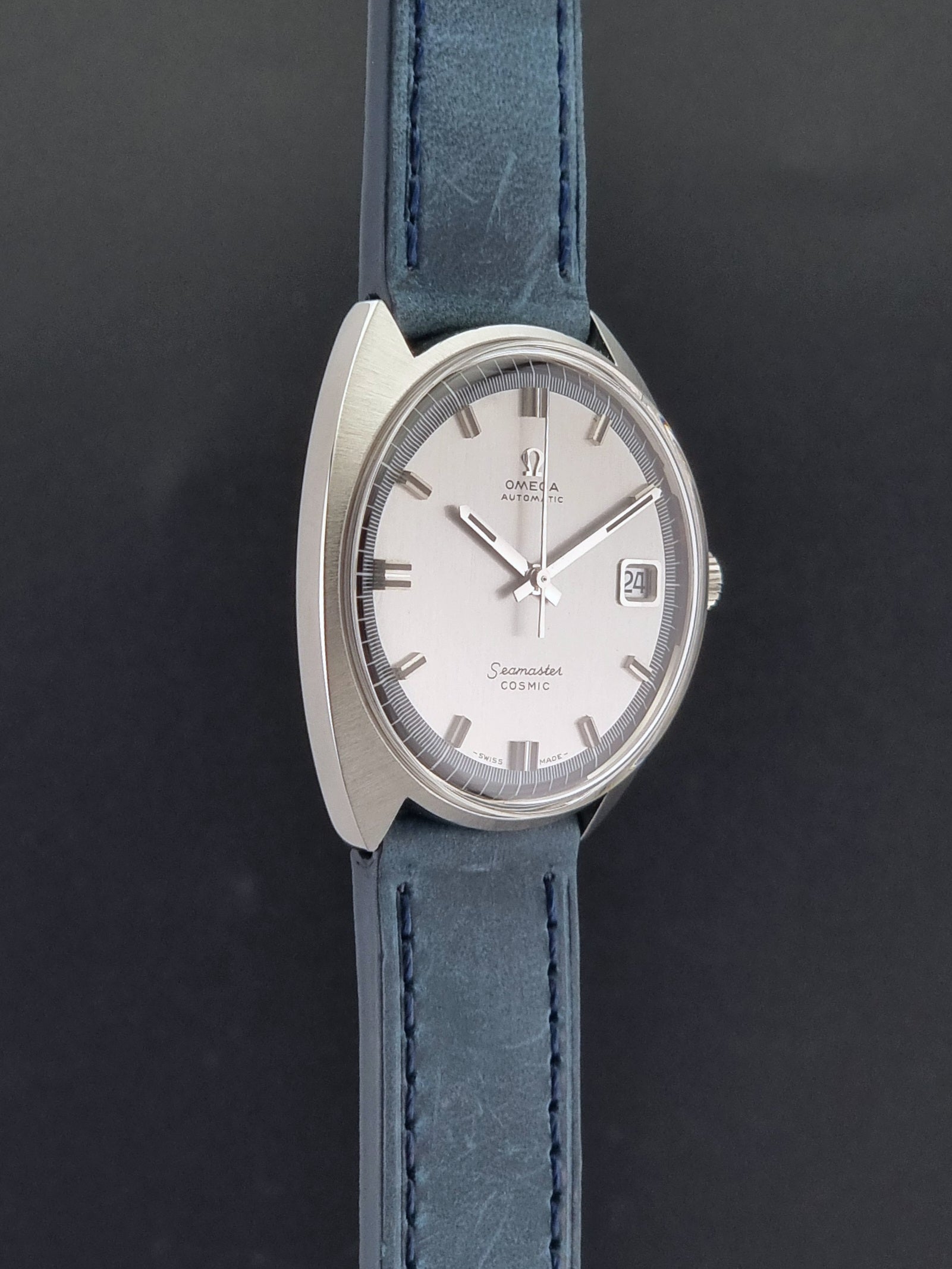 Vintage Omega 166.026 Seamaster Cosmic Wristwatch with blue leather strap and silver case on a dark gray background side profile view