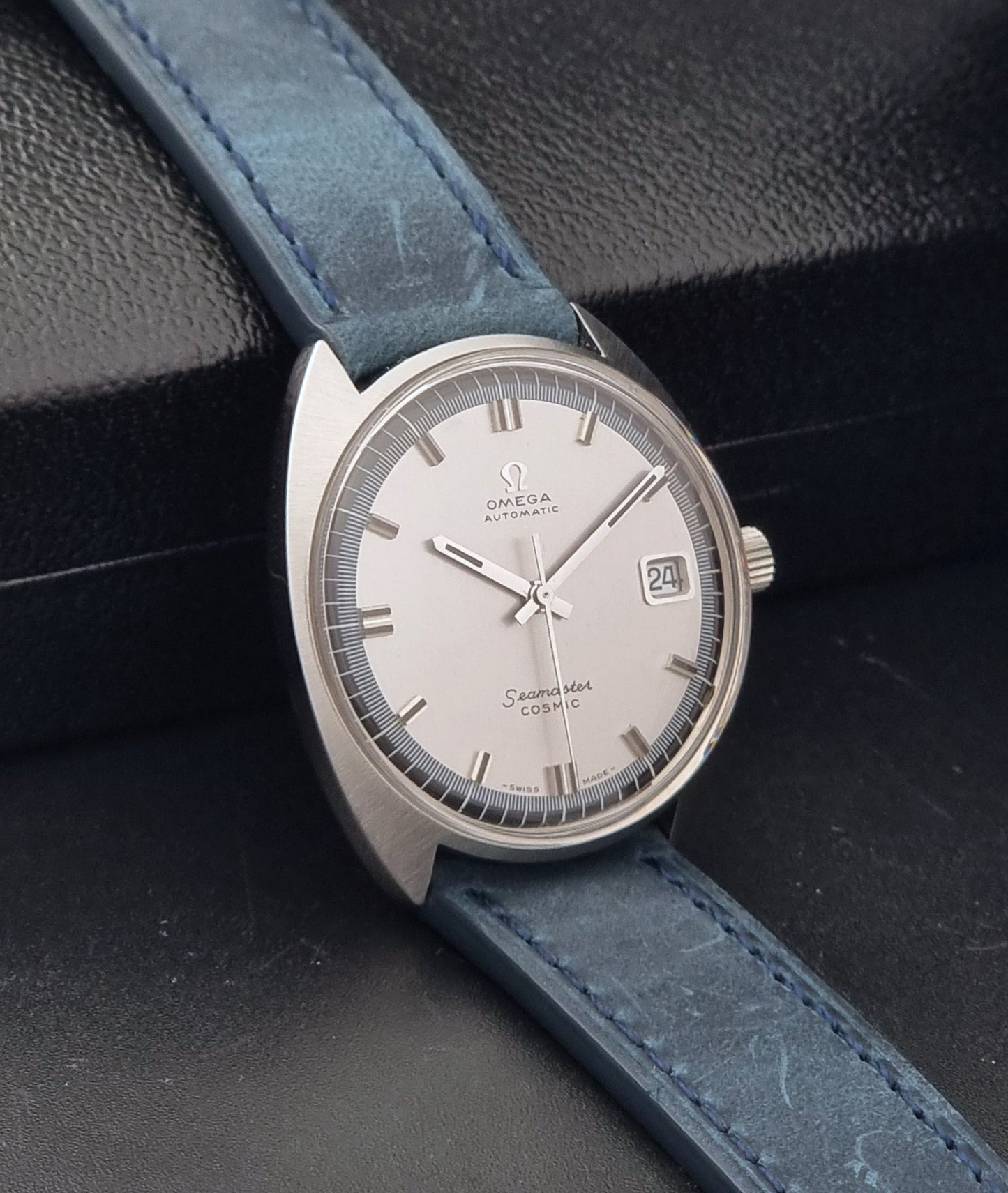 Vintage Omega 166.026 Seamaster Cosmic Wristwatch with blue leather strap and silver case on a dark gray background side view