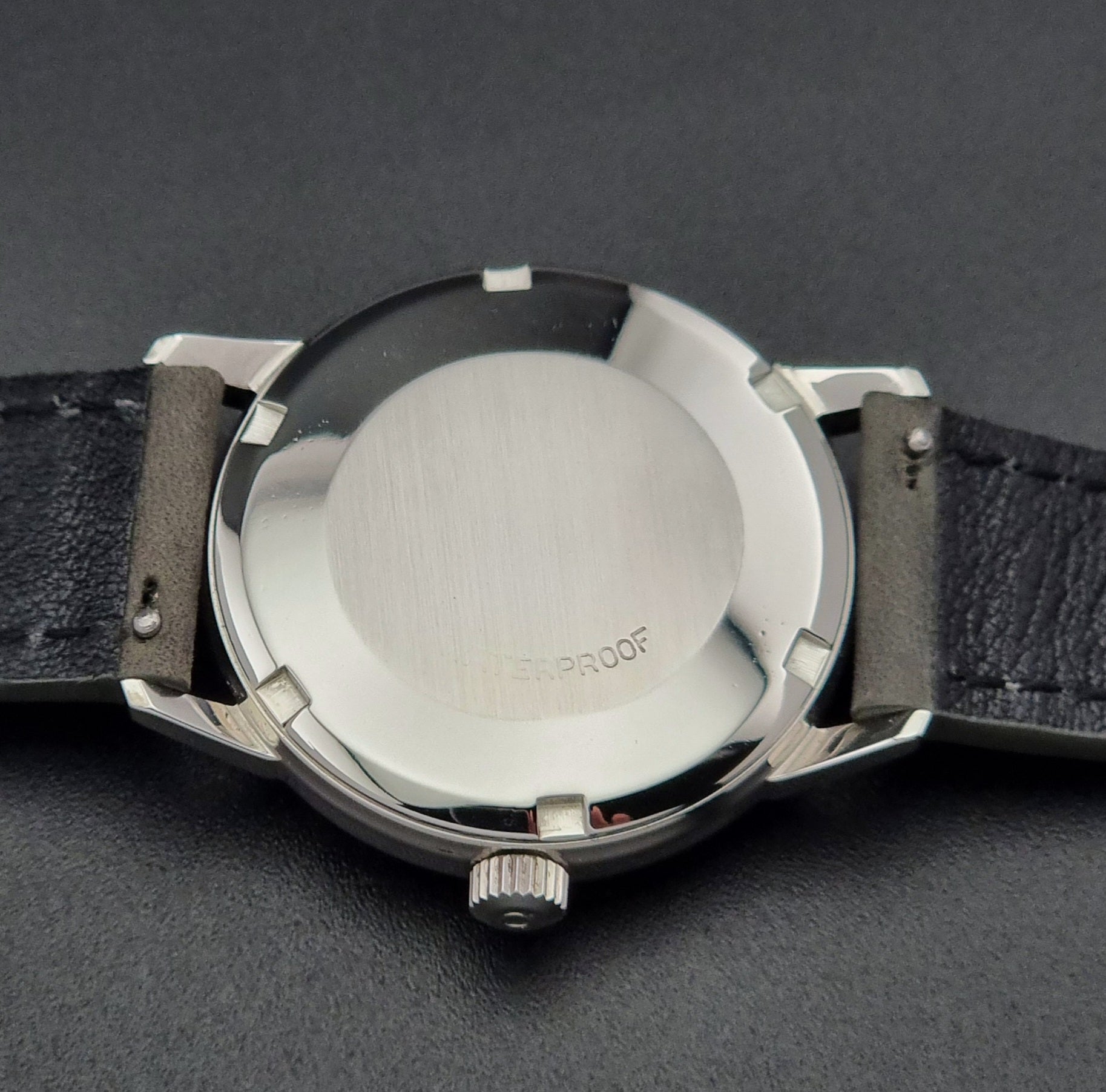 Vintage Omega Seamaster Wristwatch 166.037 with a dark leather strap on a gray background case back