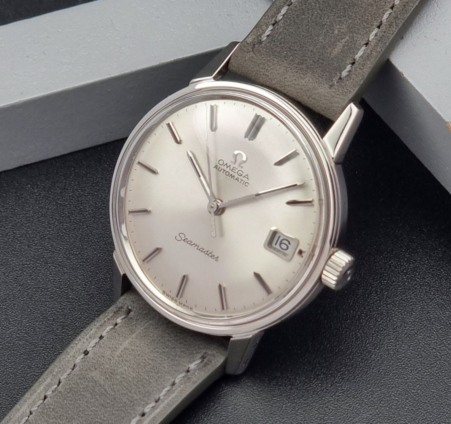 Vintage Omega Seamaster Wristwatch 166.037 with a dark leather strap on a gray background crown side