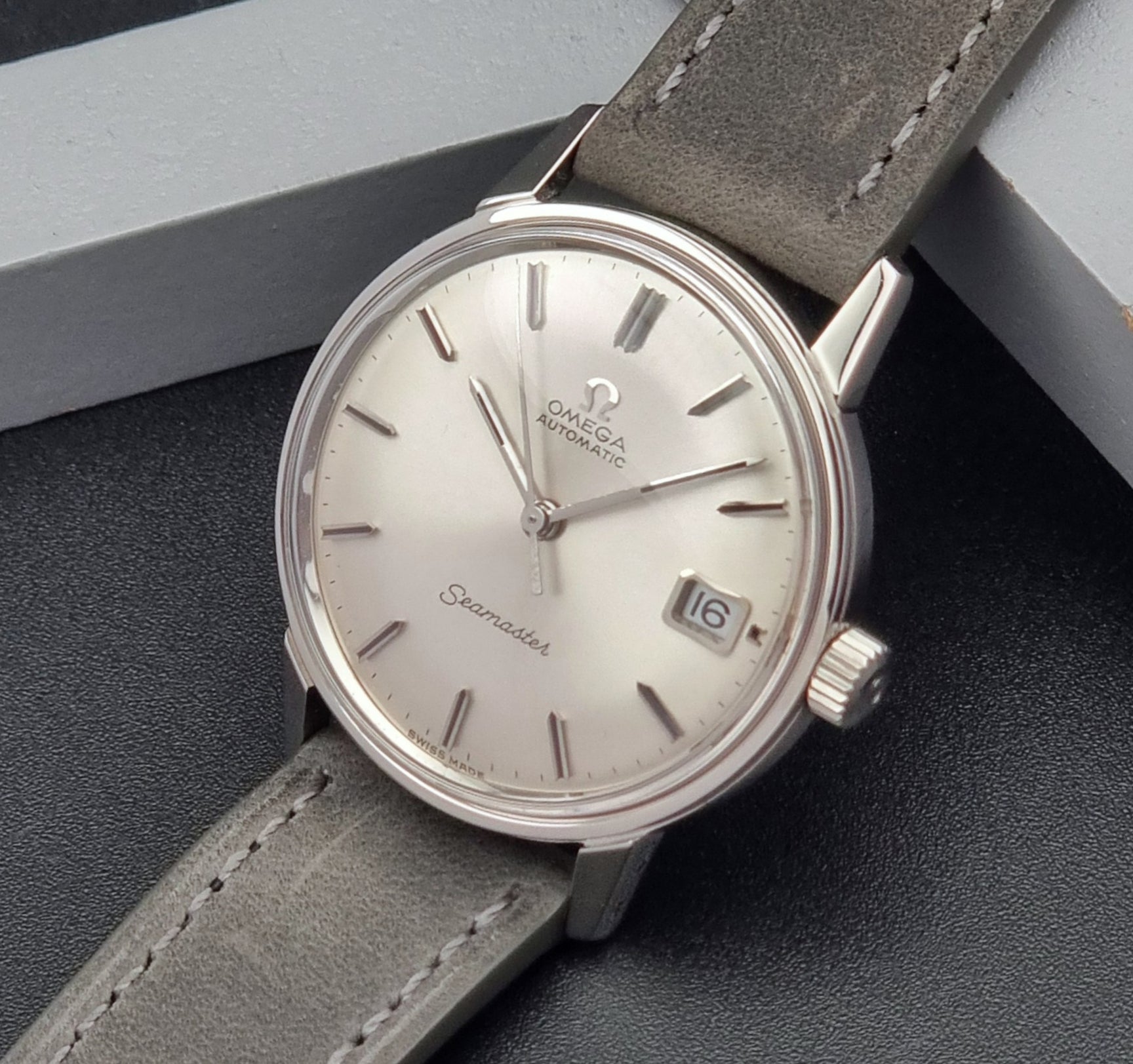 Vintage Omega Seamaster Wristwatch 166.037 with a dark leather strap on a gray background crown side