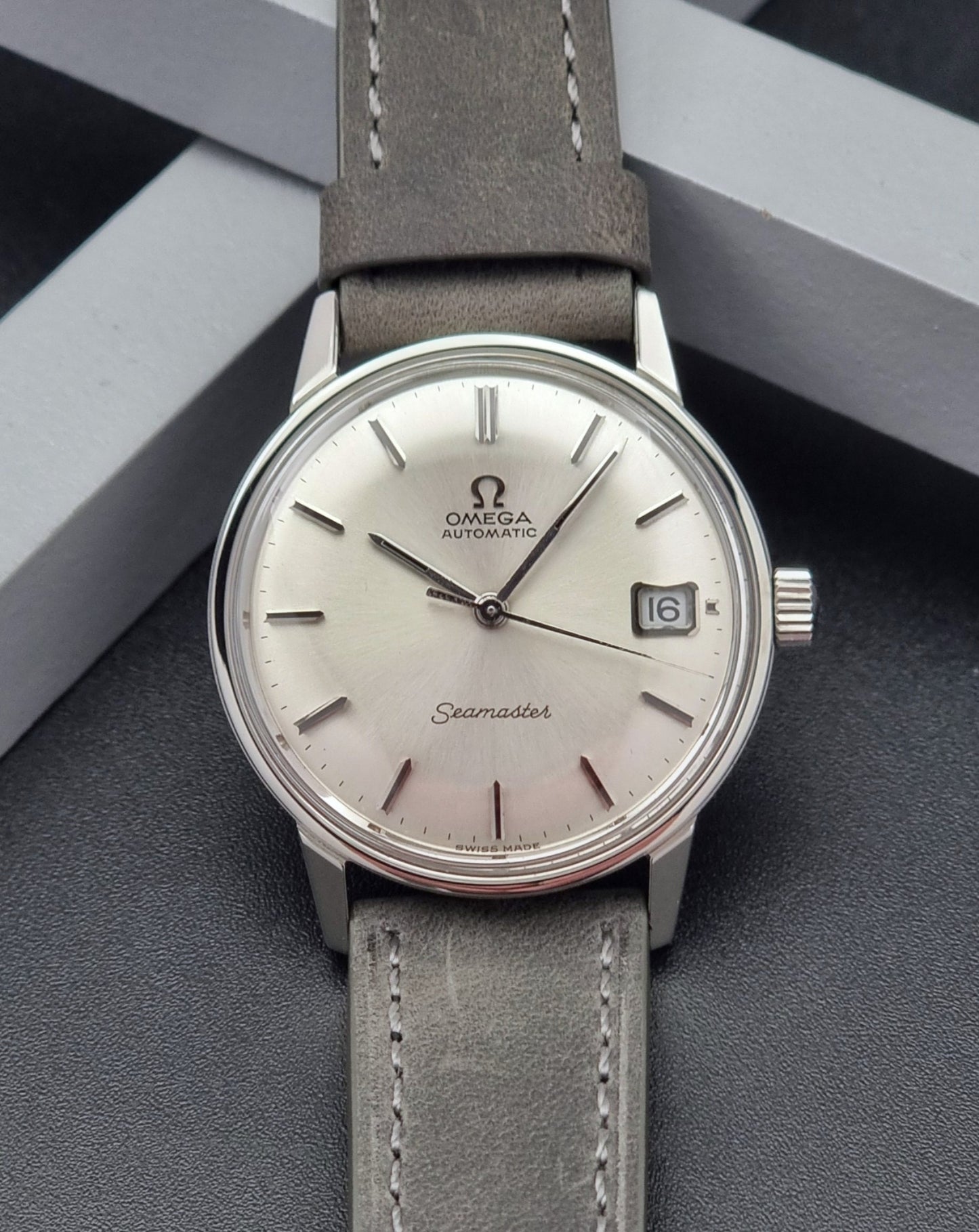 Vintage Omega Seamaster Wristwatch 166.037 with a dark leather strap on a gray background front