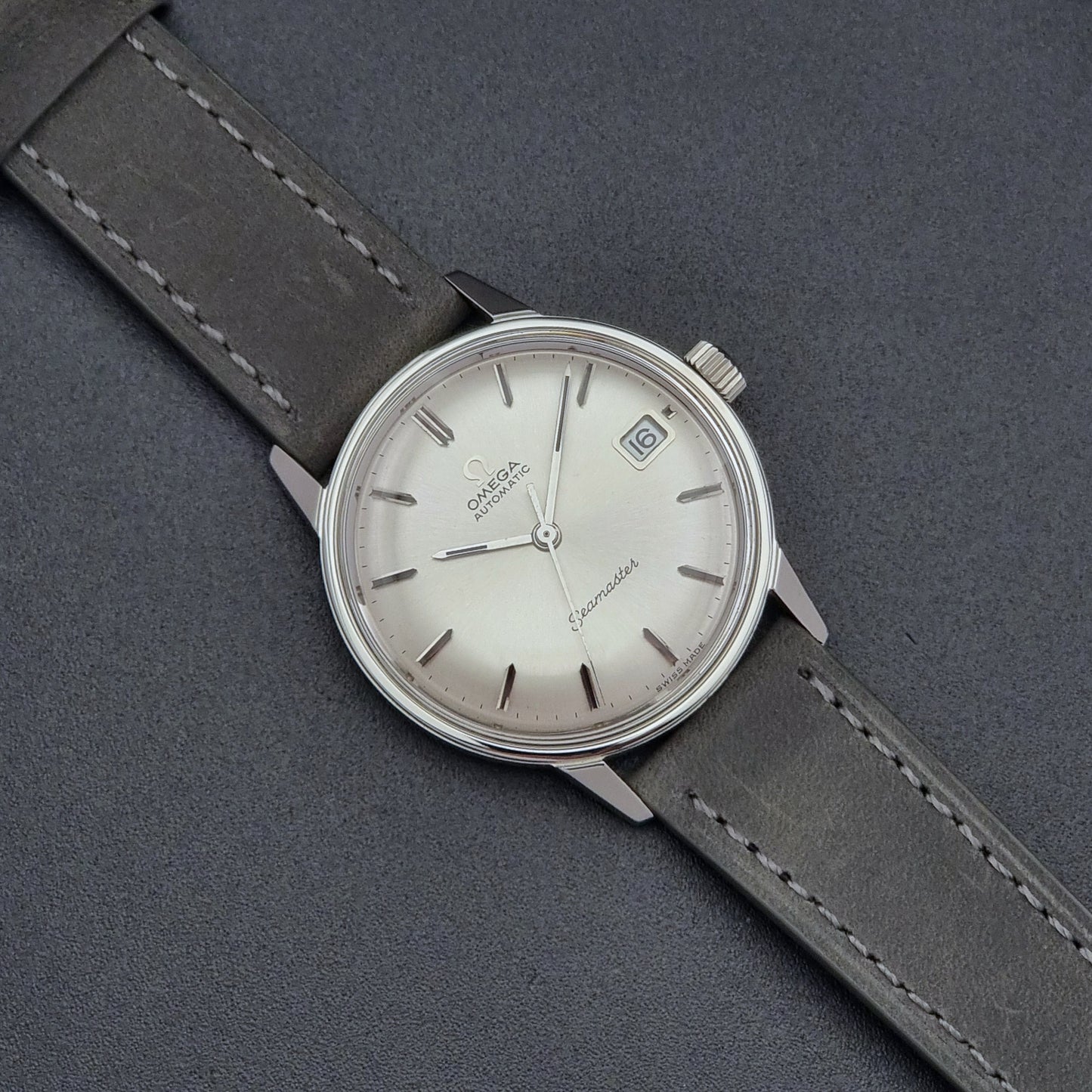Vintage Omega Seamaster Wristwatch 166.037 with a dark leather strap on a gray background