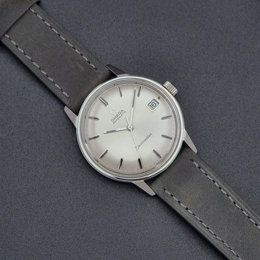 Vintage Omega Seamaster Wristwatch 166.037 with a dark leather strap on a gray background