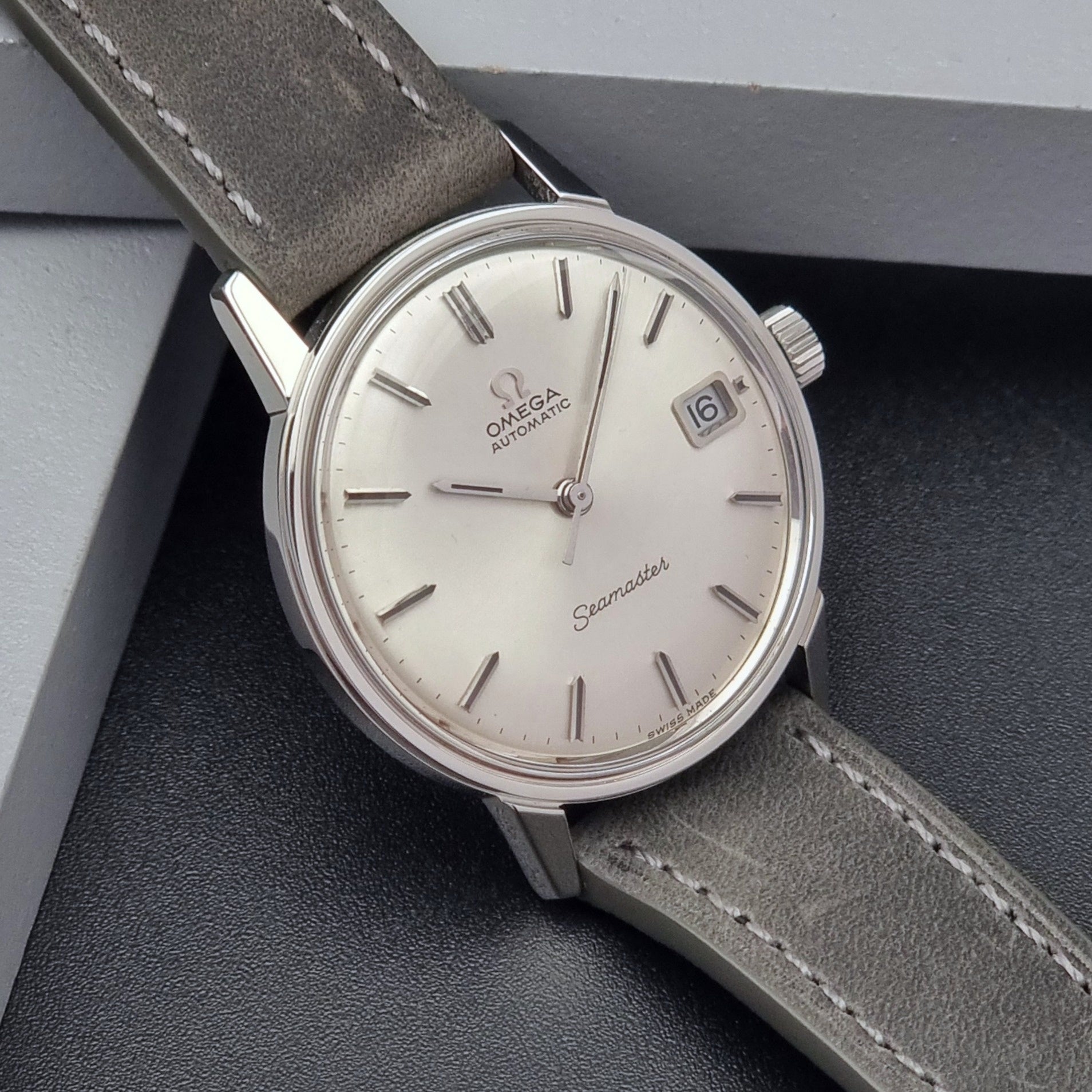 Vintage Omega Seamaster Wristwatch 166.037 with a dark leather strap on a gray background side