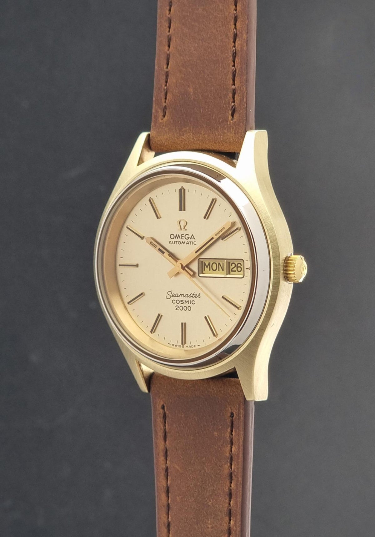 Vintage Omega Wristwatch Seamaster Cosmic 2000 Jumbo 166.129 with a gold-tone case, gold dial, and brown leather strap, shown against a dark gray background.